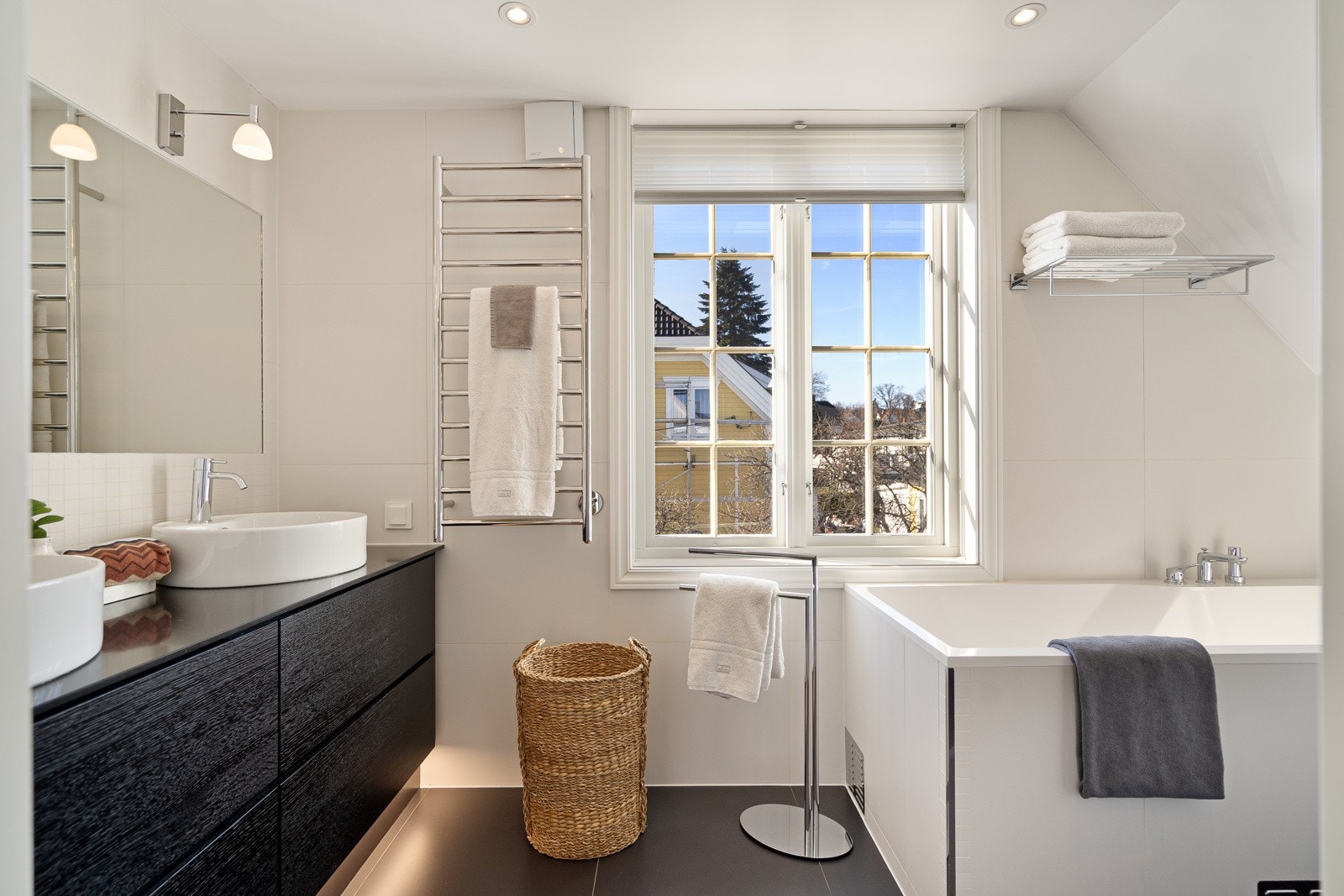 Langs den ene veggen er det etablert en sort skuffeløsning med sokkelbelysning og to toppmonterte servantskåler, plassert under et stort speil med tilhørende lampetter. Benkeplate i Silestone - alt levert av Kvik. Galleribilde