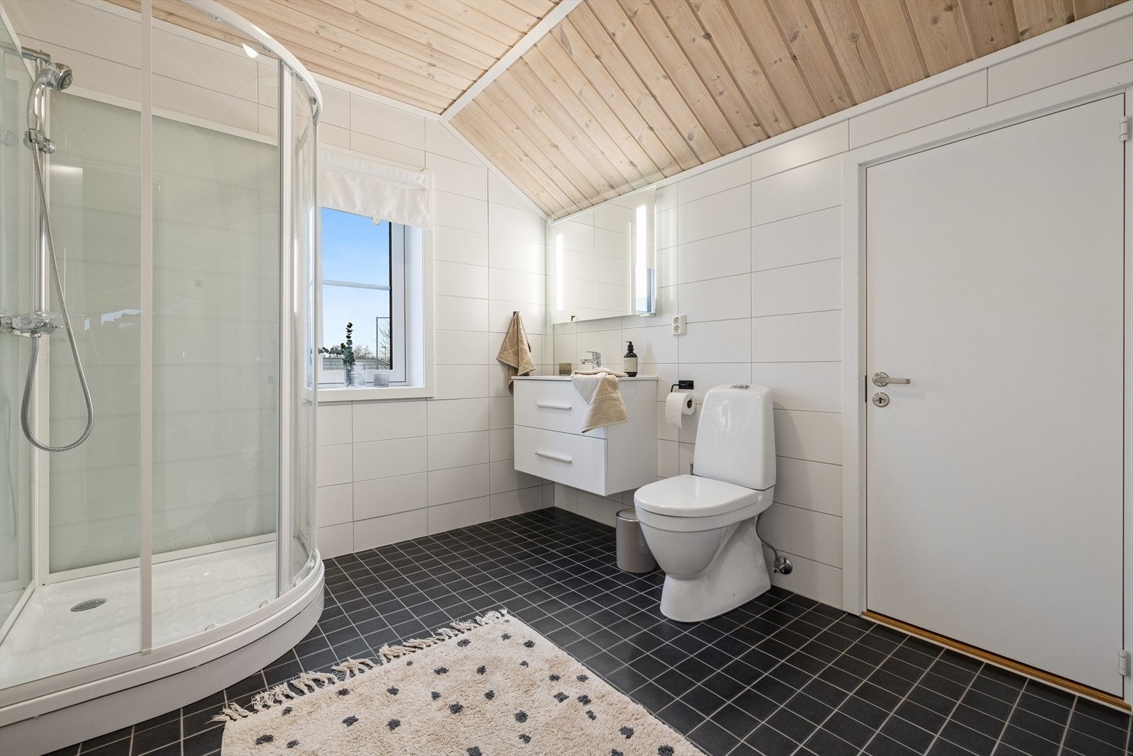 Rommet er innredet med dusjkabinett, baderomsinnredning med servant og skuffeseksjon i lys utførelse, toalett og vegghengt belyst speil. Galleribilde