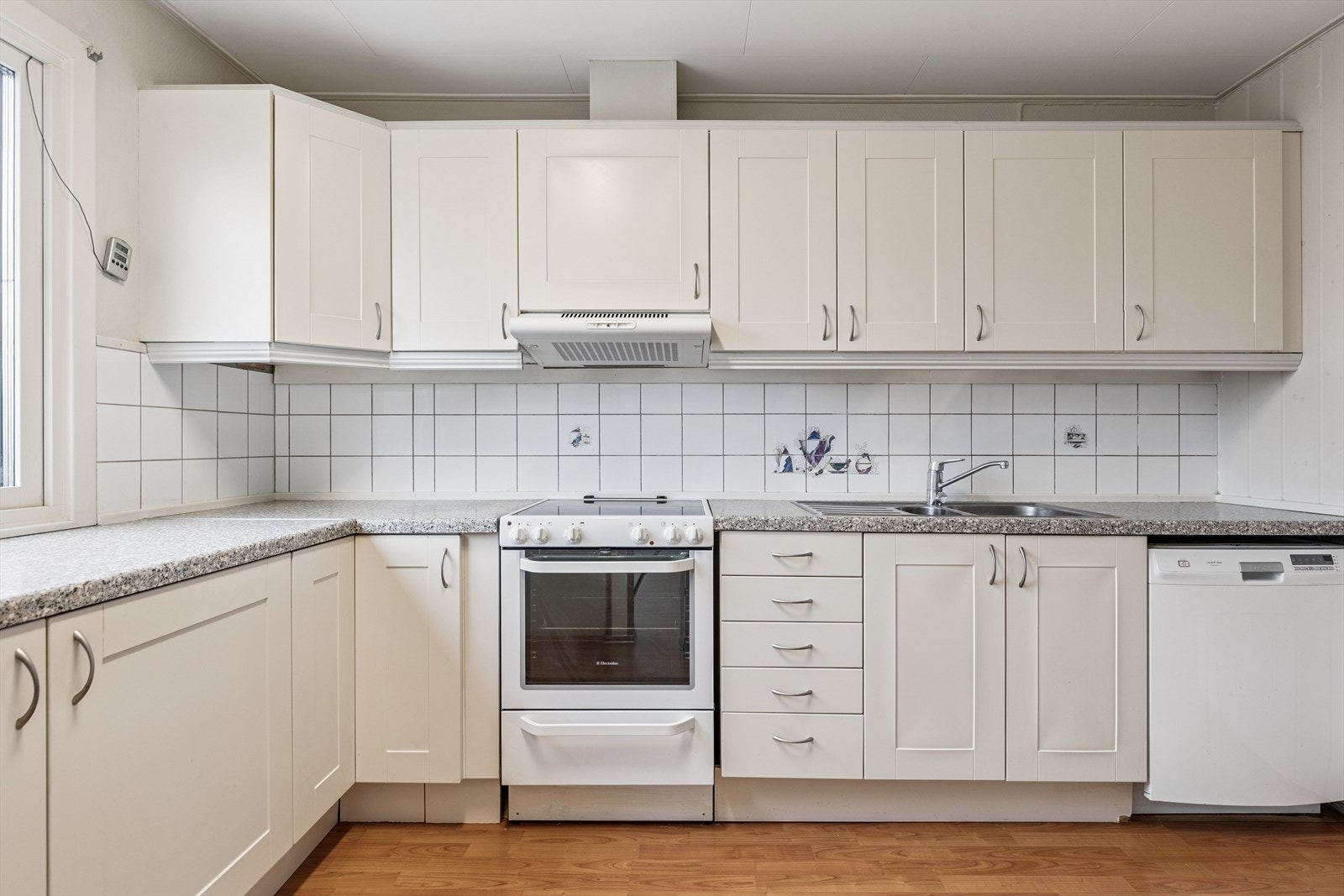 Innholdsrik kjøkkeninnredning med profilerte fronter, laminat benkeplate med nedfelt dobbel oppvaskkum og fliser mellom benk og overskap. Galleribilde