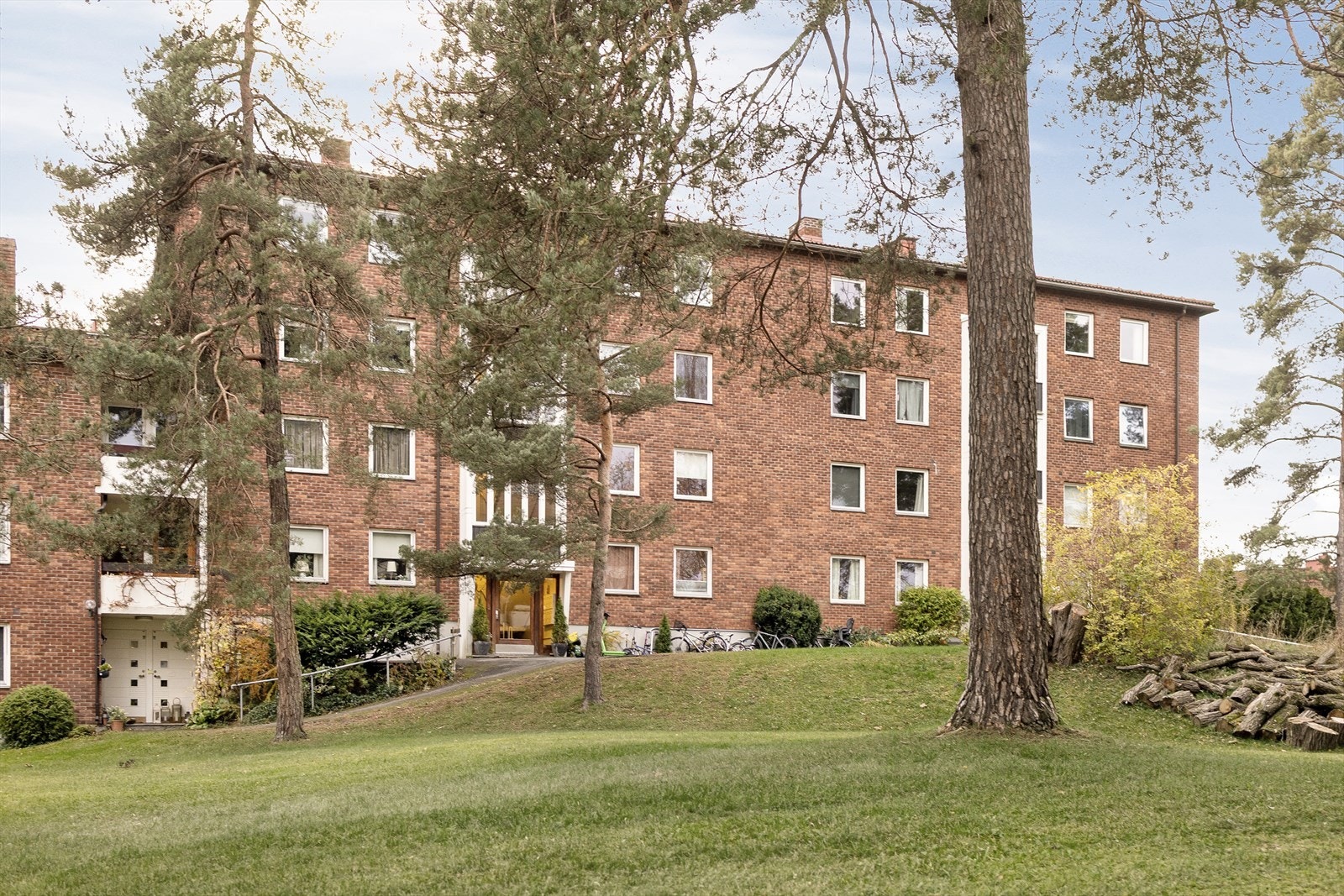 Bygningen ligger i et grøntområde med plen og høye trær som gir naturlig skjerming. Galleribilde