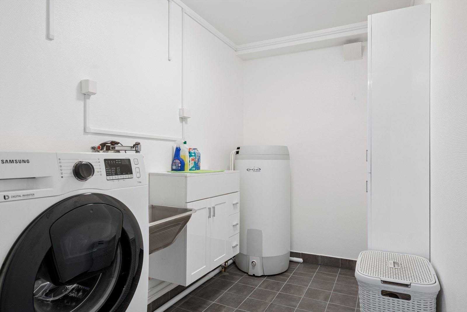 Separat vaskerom med opplegg for vaskemaskin samt utslagsvask på vegg. Flislagt gulv med varmekabler. Galleribilde