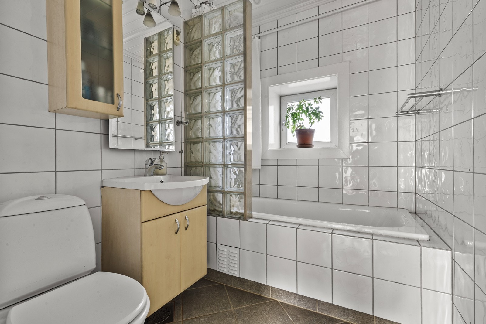 Flislagt bad med badekar, servant med tilhørende skapplass og toelett Galleribilde