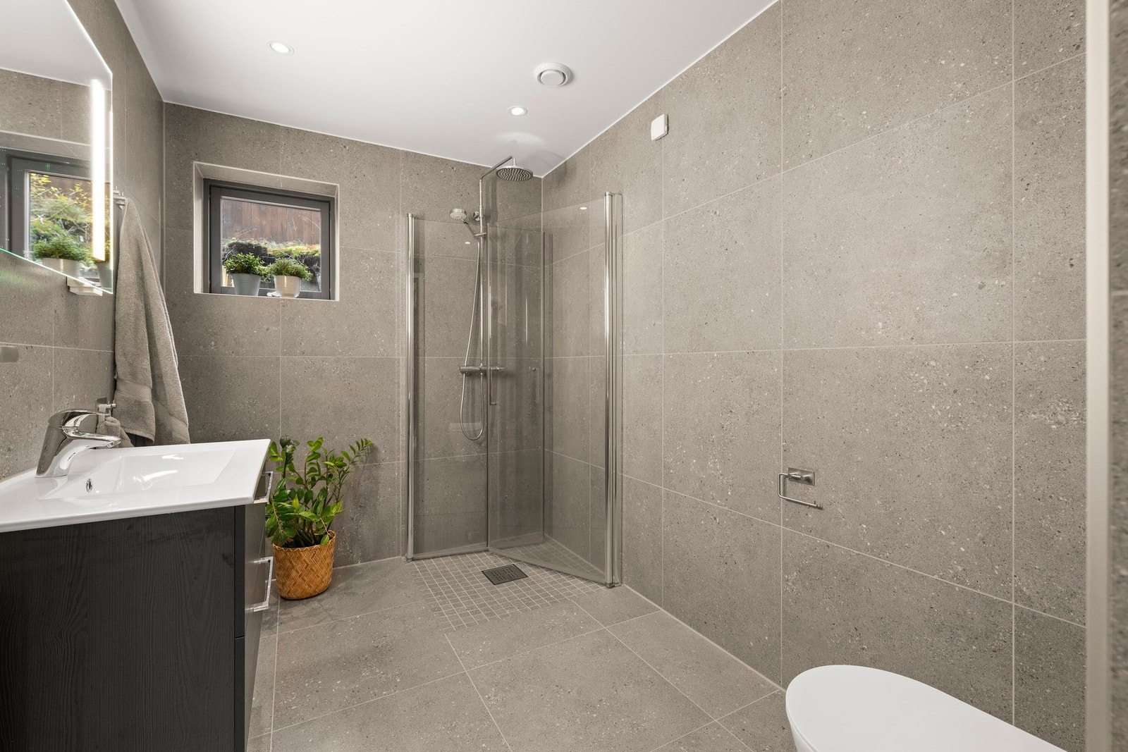 Badet er utstyrt med dusj med innfellbare dører i herdet glass, veggfestet klosett med innebygget sisterne og servant i helstøpt plate. Galleribilde