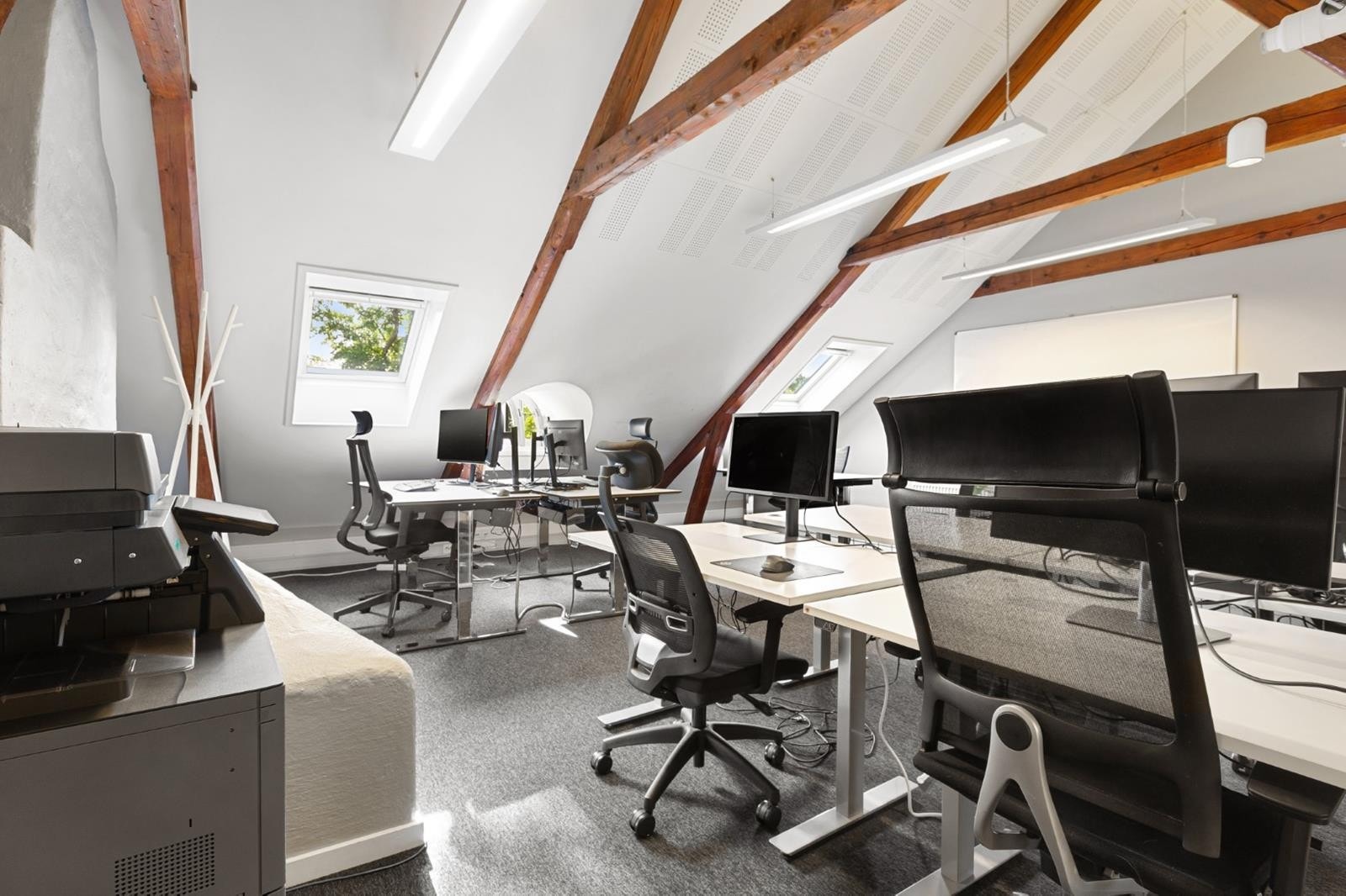 Kontorlandskap under takbjelkene. God takhøyde, lysinnslipp fra takvinduer og plass til flere arbeidsstasjoner. Et kreativt miljø som kombinerer sjarm og funksjonalitet, perfekt for teamarbeid. Galleribilde