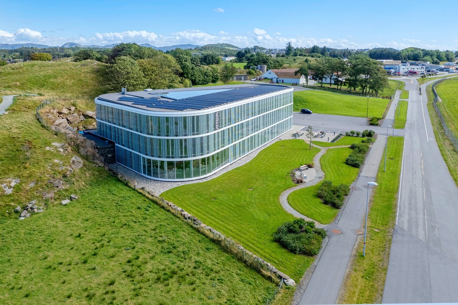 Moderne kontorbygg med buet design og solcellepaneler. Naturskjønn beliggenhet med flotte grøntområder og enkel adkomst til vei. Galleribilde