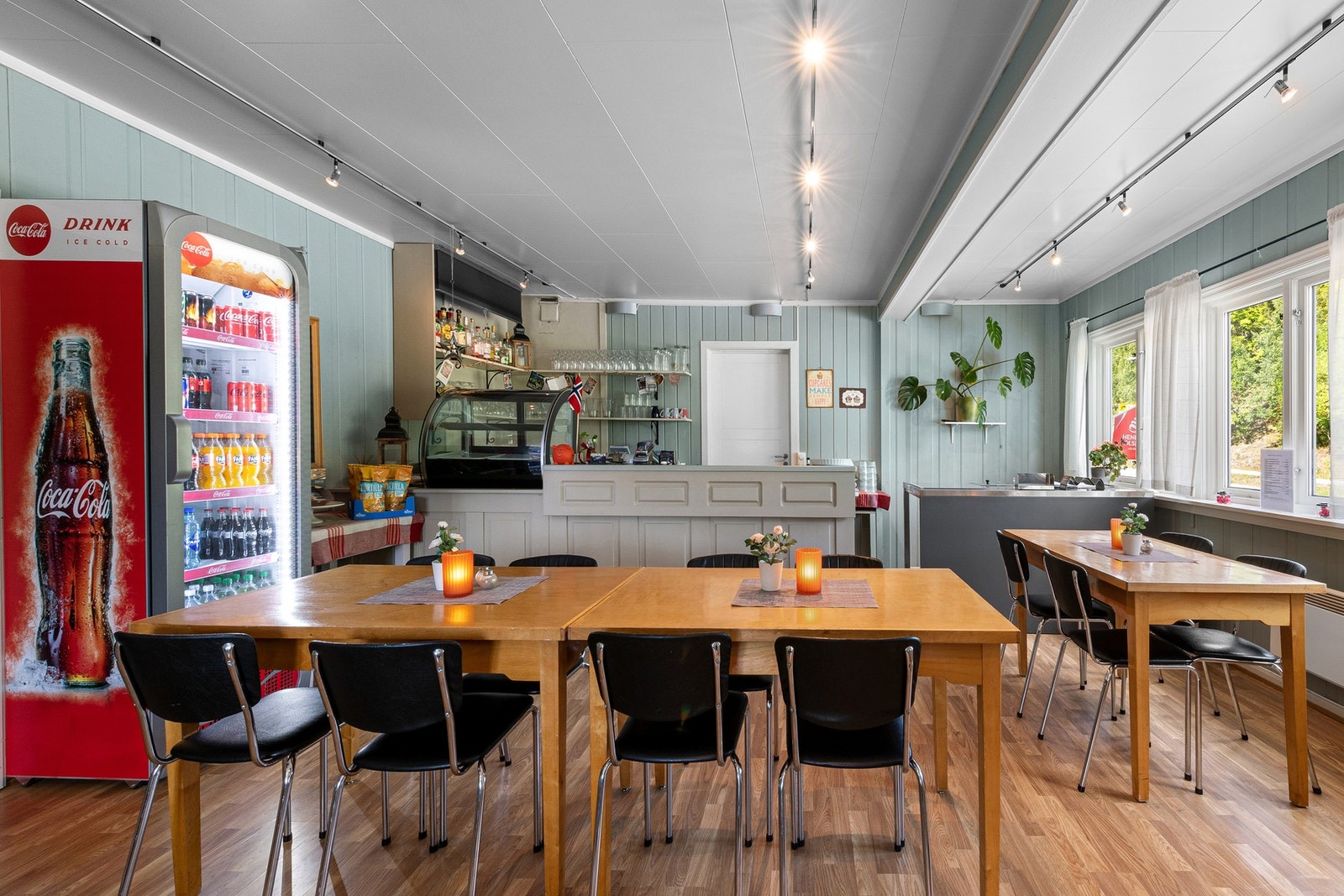 Kafeen er malt i en dus grønntone som står godt til laminatgulvet, og bak en grå bardisk i heltre er det åpne hyller og enkelt kjøkken. Galleribilde