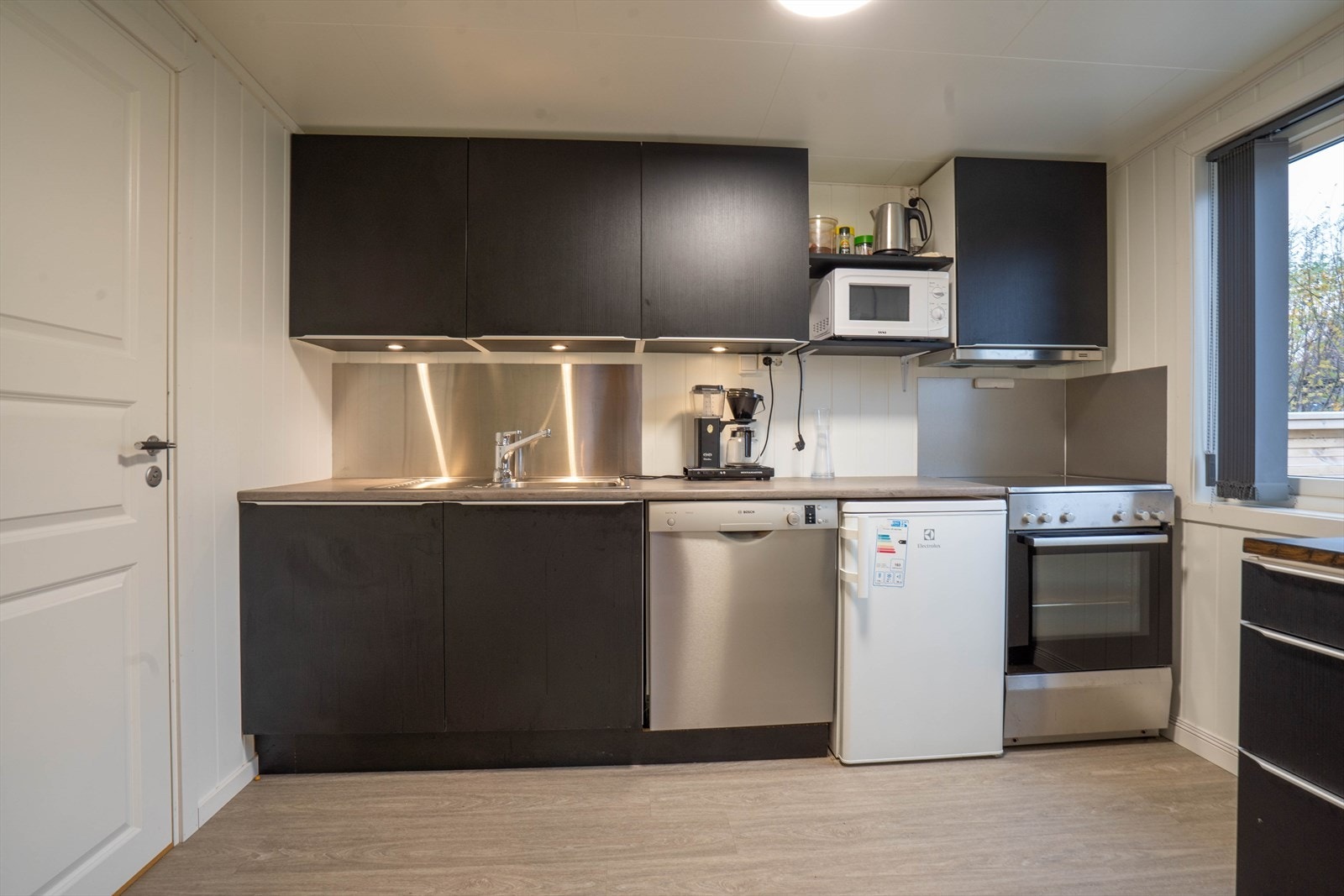 Moderne kjøkken med integrerte hvitevarer og stilrene, mørke skap. Praktisk design med godt lysinnslipp fra vindu. Galleribilde