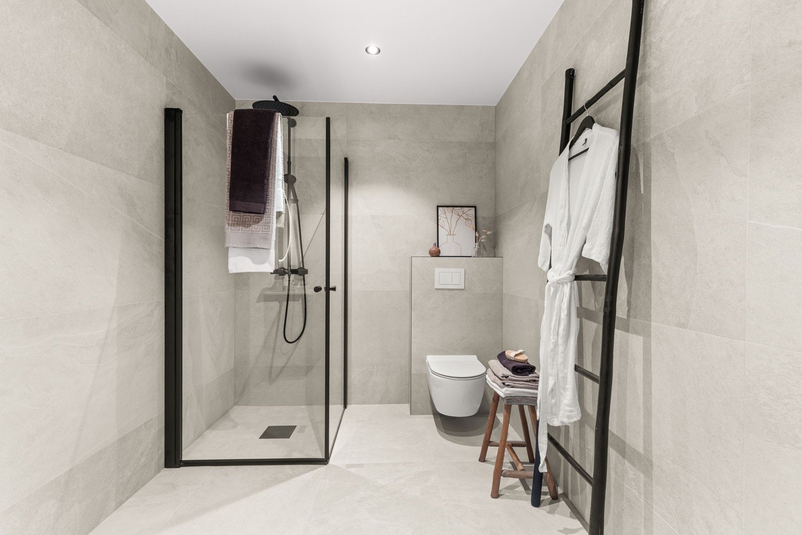 Lekkert bad med flislagt gulv og varmekbaler, dusjhjørne med glassvegger og moderne detaljer i sort utførelse. Galleribilde