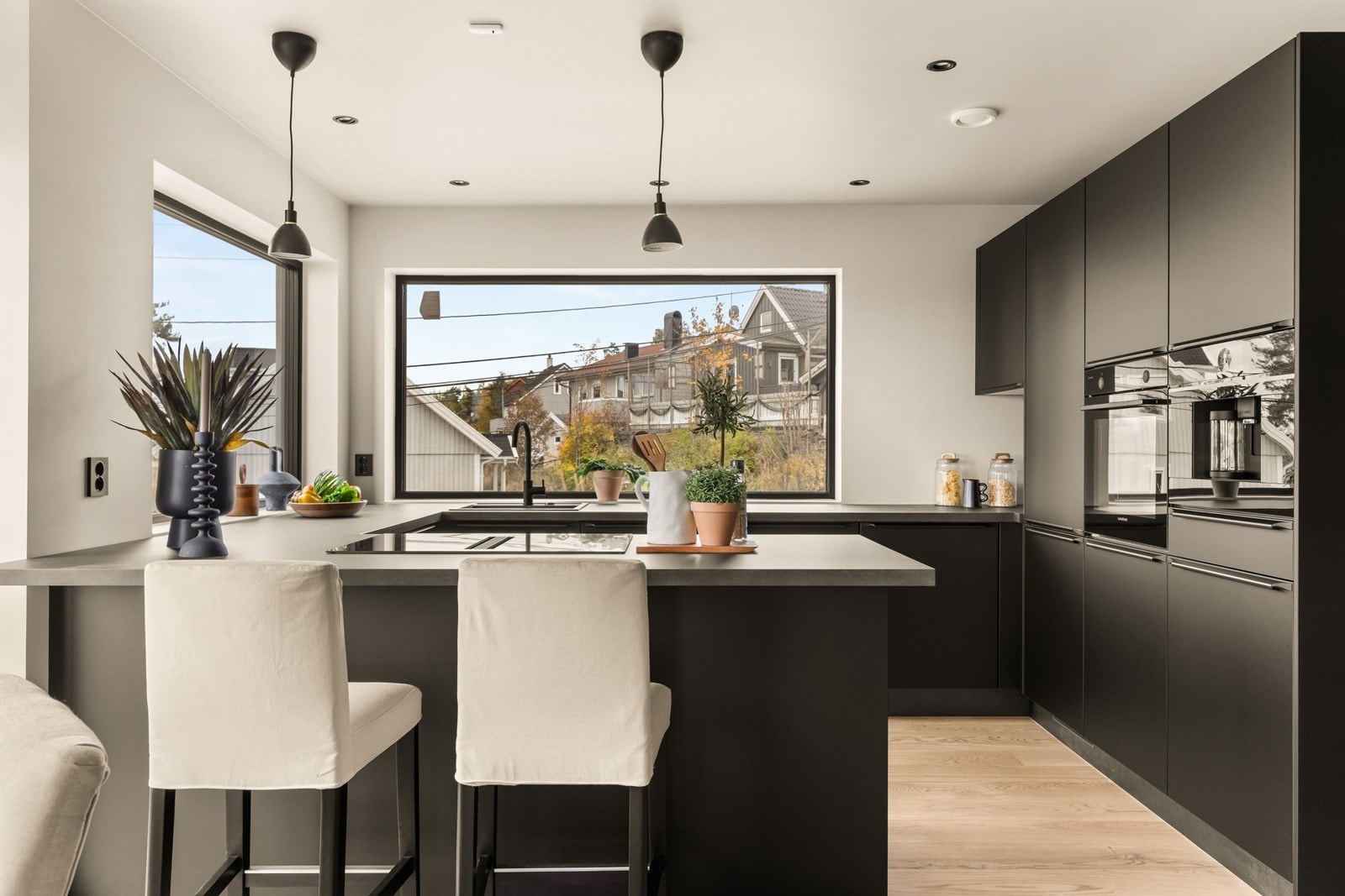 Moderne kjøkken med stilrene, mørke fronter og kjøkkenøy som skaper et naturlig skille fra stuen. Galleribilde