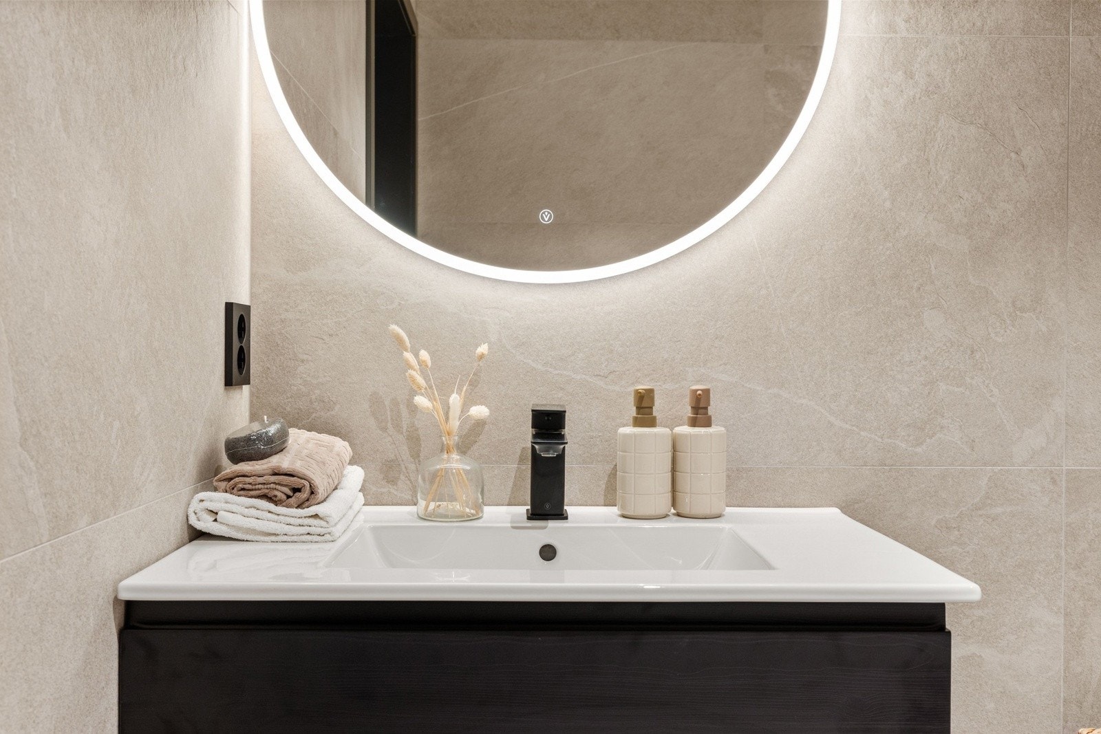 Delikat baderomsinnredning med mørke fronter, rundt speil og tidløse materialvalg. Galleribilde