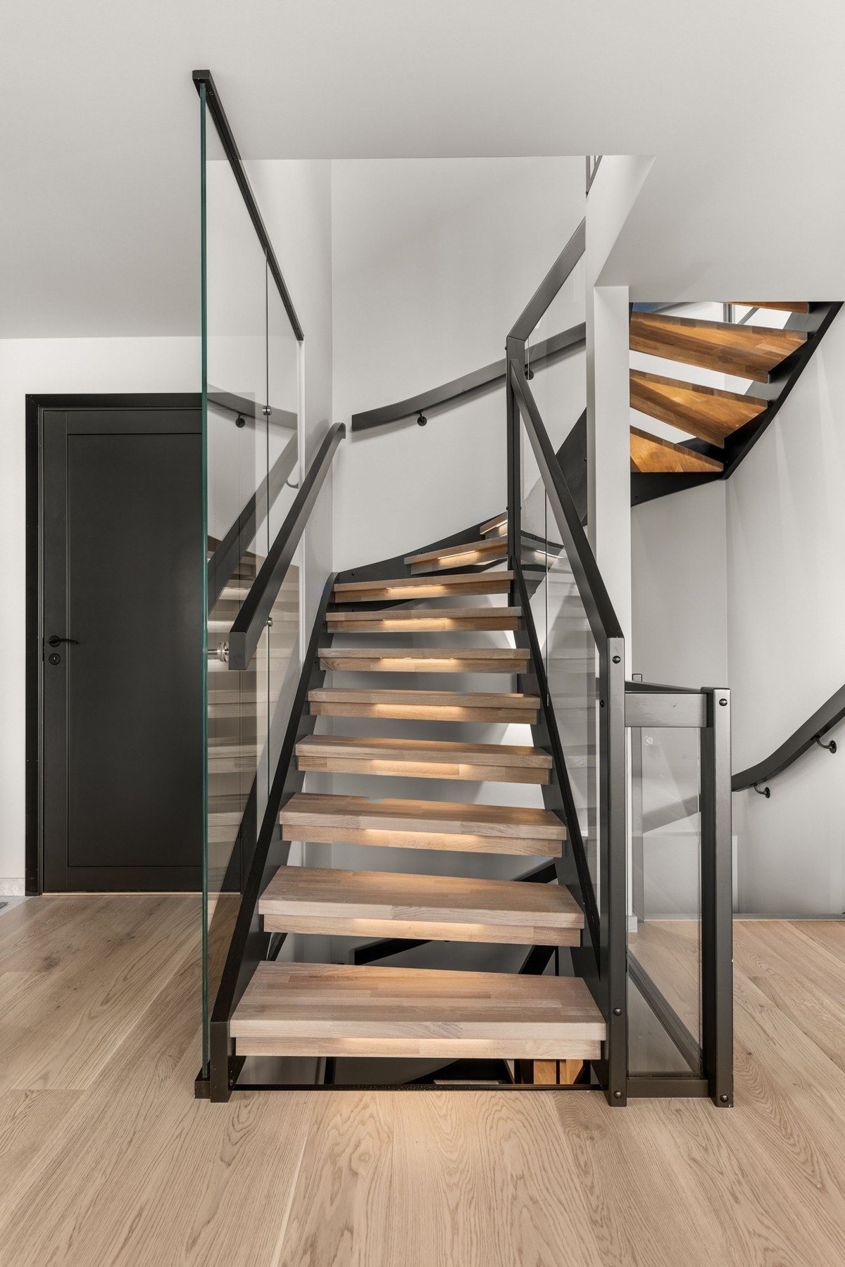 Innvendig trapp med hvitlaserte trinn i hardved og rekkverk i glass og stål, et stilrent blikkfang som binder etasjene elegant sammen. Galleribilde