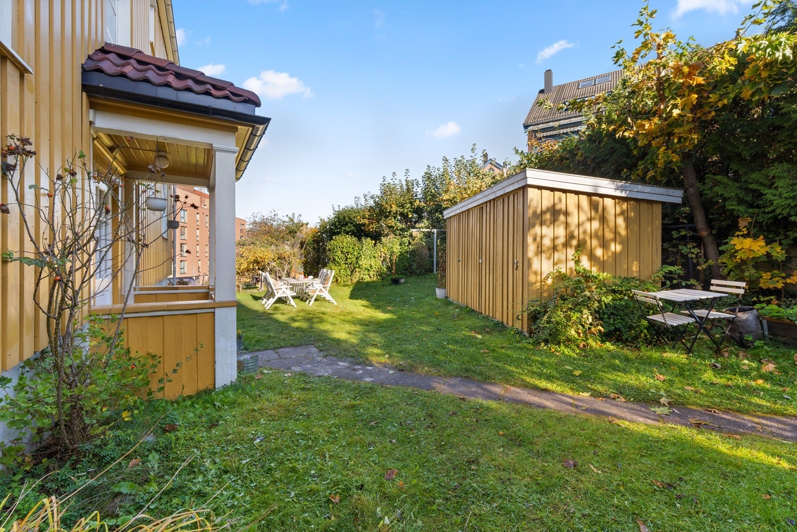 Vakker felles hage med sittegrupper og lekeområde og et uthus hvor leiligheten har sin egen utebod. Galleribilde