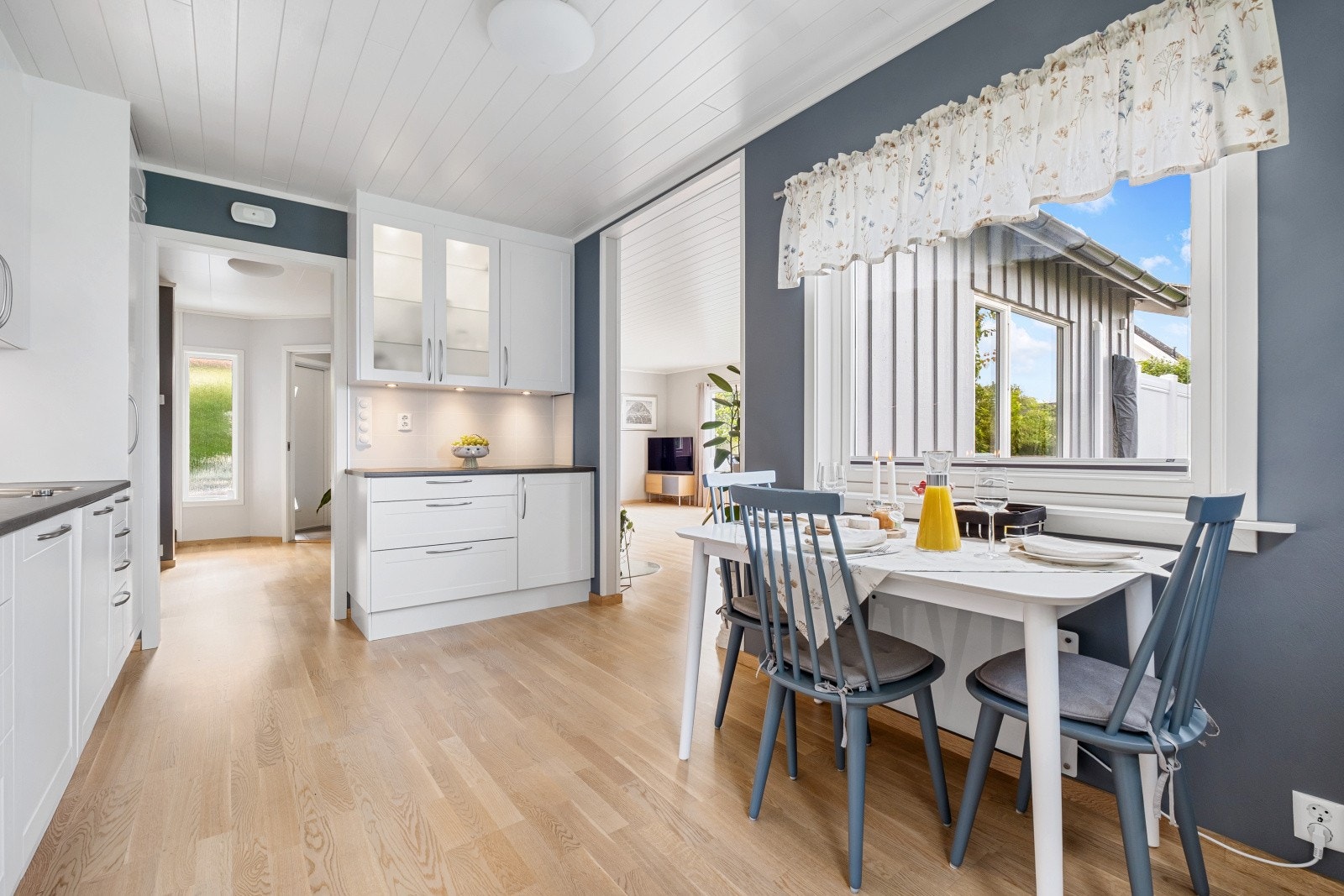 Kjøkkenet har en stilren innredning fra Nettoline med hvite profilerte fronter, mørk benkeplate med nedfelt kjøkkenvask og Kitchenboard på vegg over benk Galleribilde