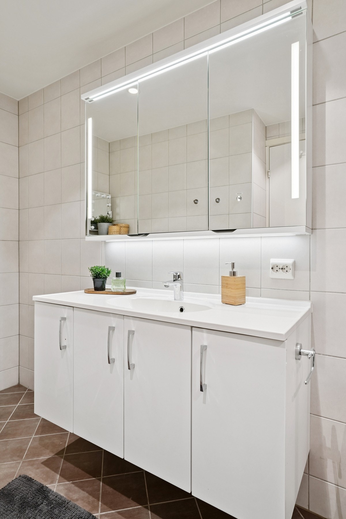 Badet har innredning med hvite glatte skapfronter og helstøpt servant. Skapspeil med belysning over. Galleribilde