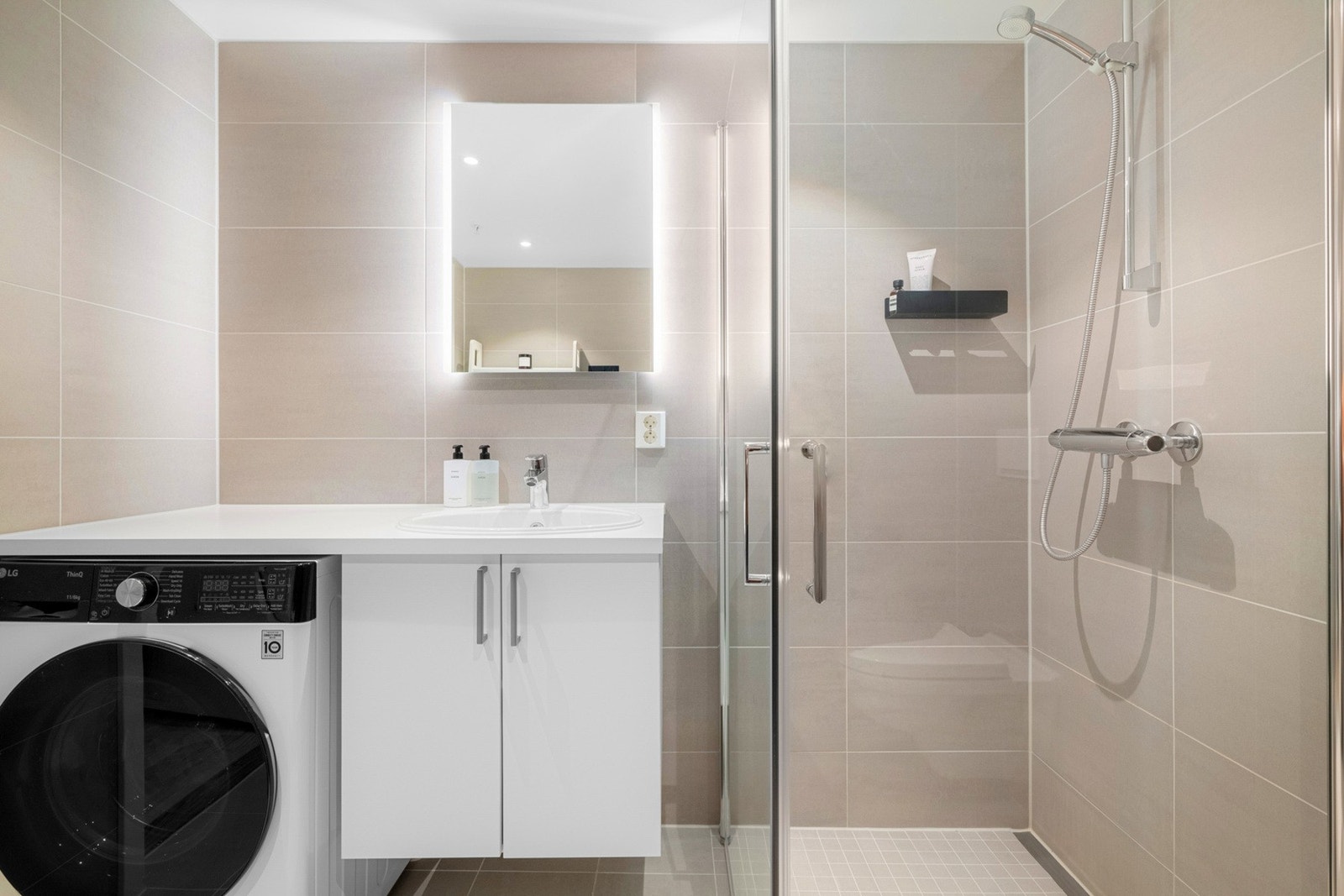 Pen og praktisk baderomsinnredning med servant med ettgreps blandebatteri og opplegg for vaskemaskin / tørketrommel Galleribilde