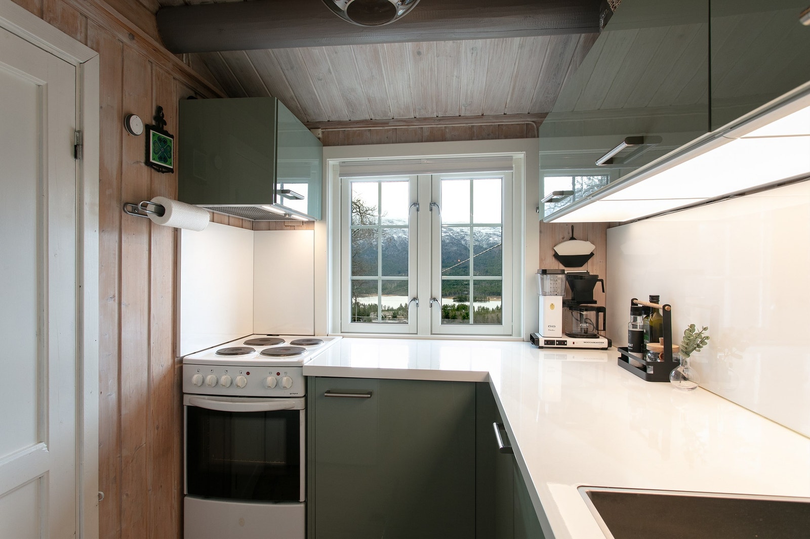 Kjøkkenet har grågrønne fronter og hvit benkeplate av laminat med nedfelt oppvaskkum med ett-greps kjøkkenarmatur. Integrert oppvaskmaskin, frittstående komfyr samt kjøl/fryseskap. Hvitevarer medfølger Galleribilde