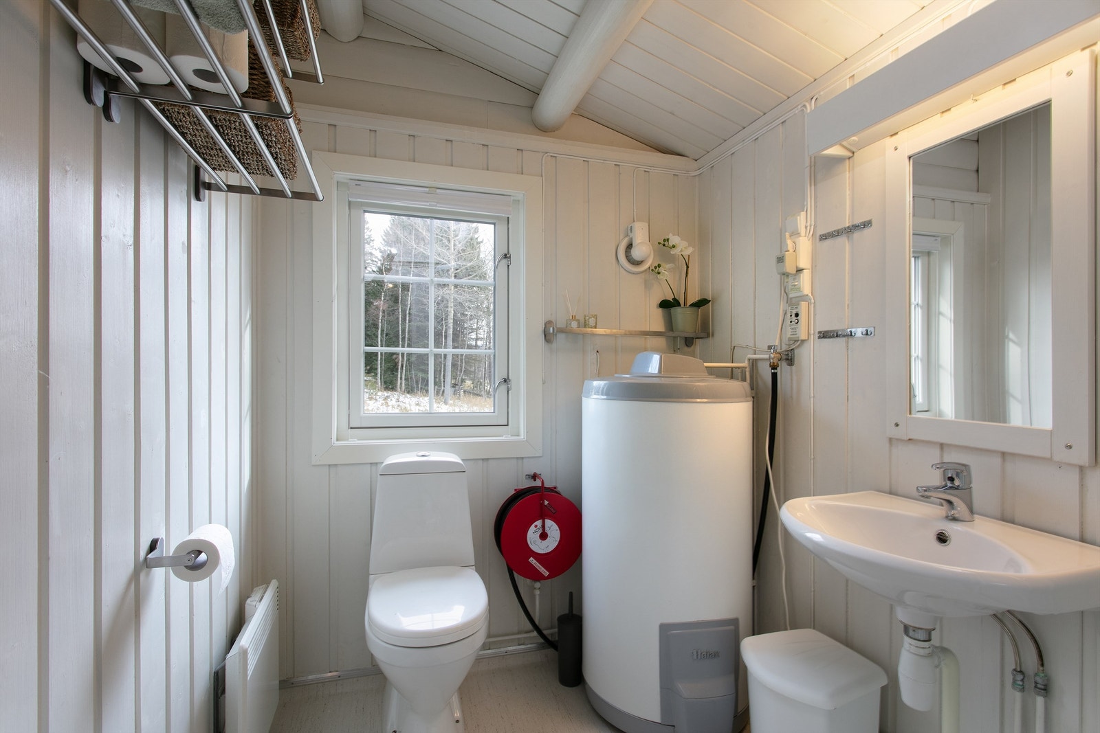 Bad med frittstående toalett, servant, speil med overlys, v.v.bereder plassert i hjørne. Frittstående dusjkabinett. Galleribilde