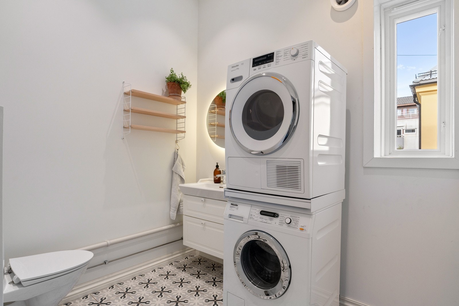 Praktisk vaskerom med opplegg for vaskemaskin, historiske fliser med varmekabler i gulvet, malte vegger og åpne rørføringer. Galleribilde