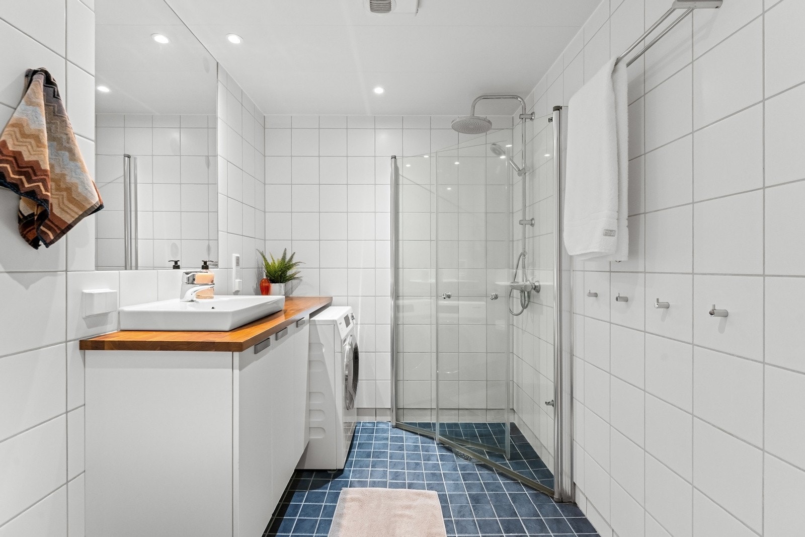 Flislagt baderom fra byggeår utført i lyse fliser med downlights i himling. Nedsenket dusjhjørne med innfellbare glassdører og regnfallsdusj Galleribilde