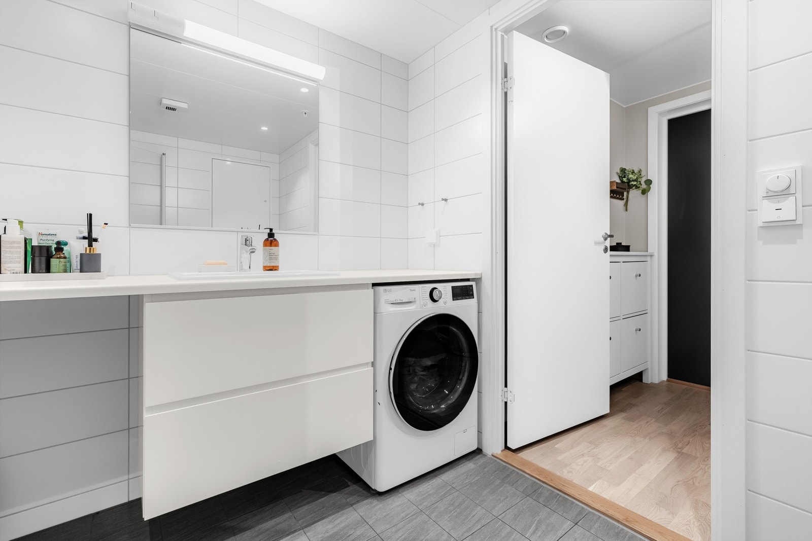 Lyst og stilrent bad med servantseksjon med skuffer, stort speil og opplegg for vaskemaskin - alt du trenger samlet på ett sted. Galleribilde