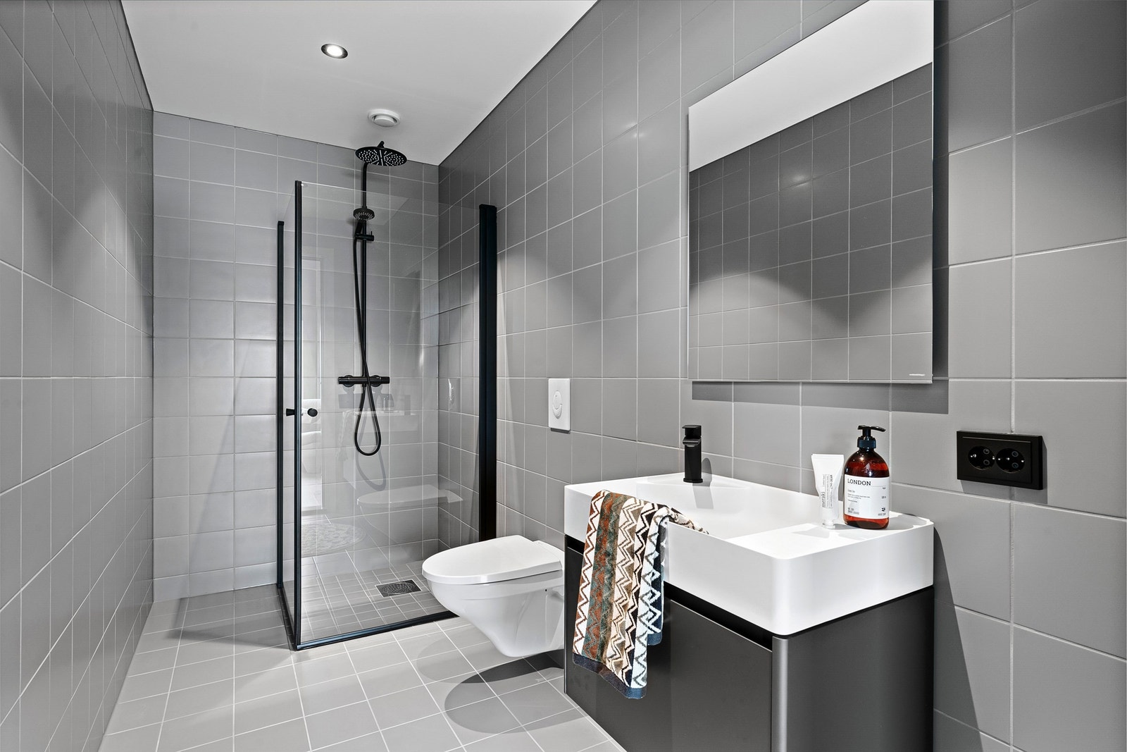 Lekkert helfliset bad med vegghengt toalett og dusjhjørne med innfellbare glassdører, sort dusjgarnityr med regnfallsdusj og baderomsinnredning fra anerkjent kvalitetsprodukt Antoniolupi. Galleribilde