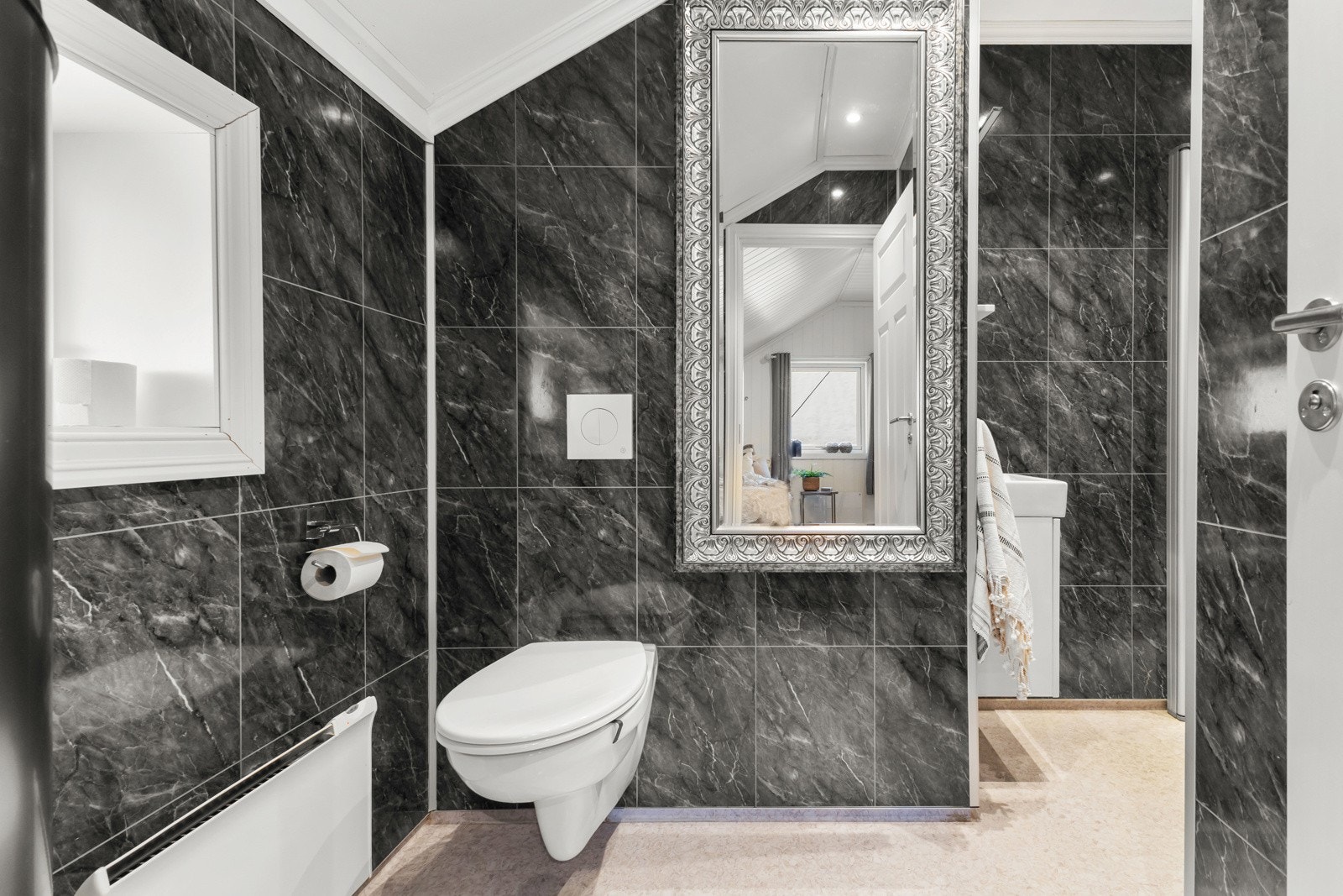 Badet ble oppusset i 2016 og har moderne baderomsinnredning med servant og underskap, dusjhjørne med glassdører, samt vegghengt toalett. Gulvet er belagt med gulvbelegg, veggene har stilrene baderomsplater, og taket er malt og utstyrt med downlights. Galleribilde