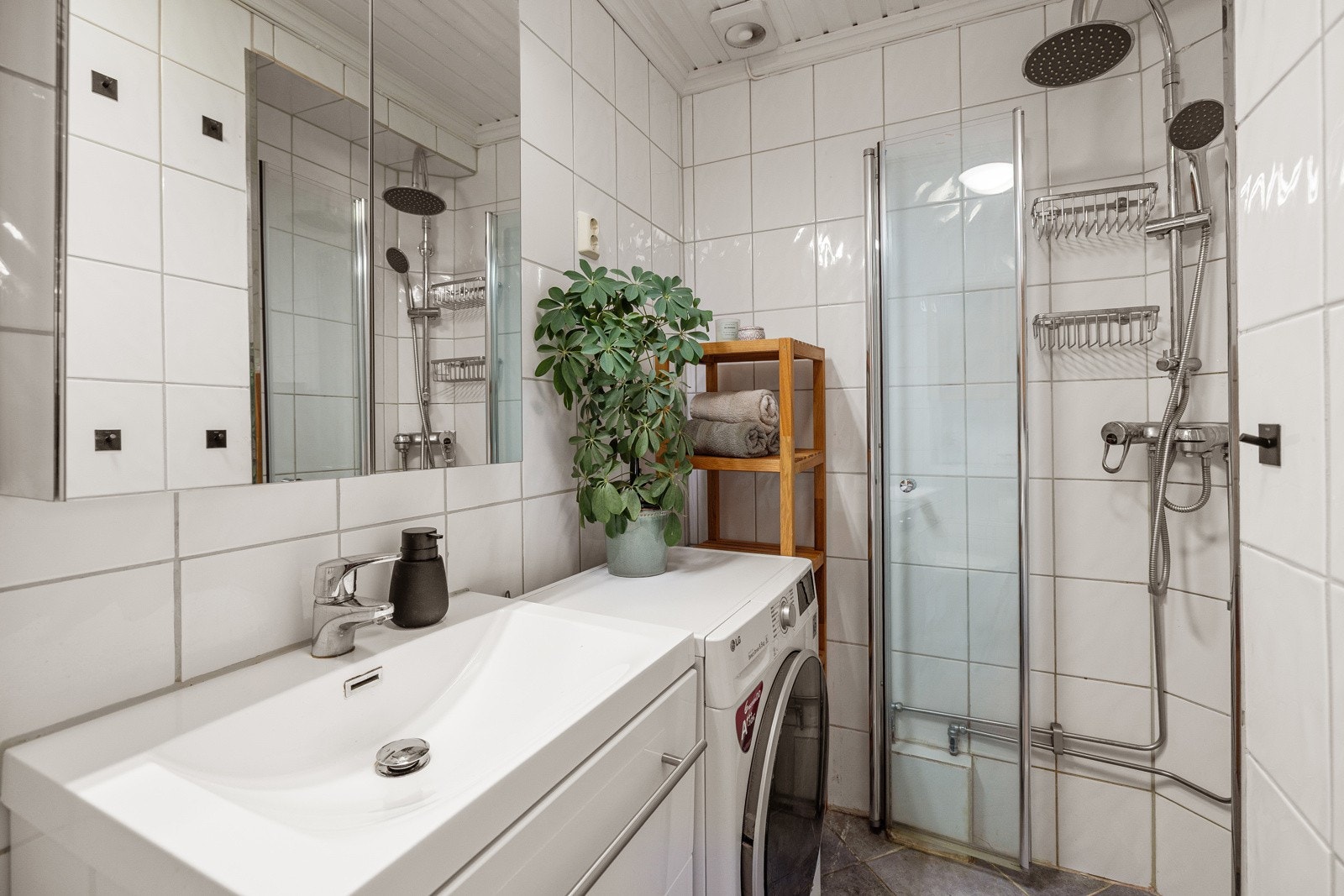 Moderne baderomsinnredning med skuffer og heldekkende servant, speilskap med belysning over. I hjørnet er det plass og opplegg for vaskemaskin. Galleribilde