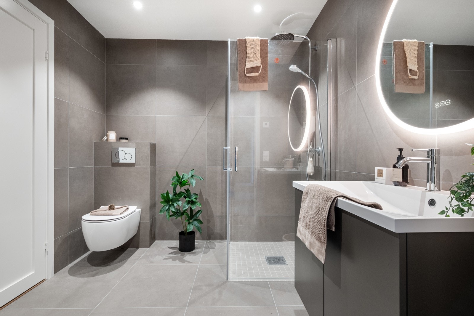 Delikat og helfliset baderom med dusjnisje, vegghengt toalett, servant med skuffeseksjon og høyskap Galleribilde