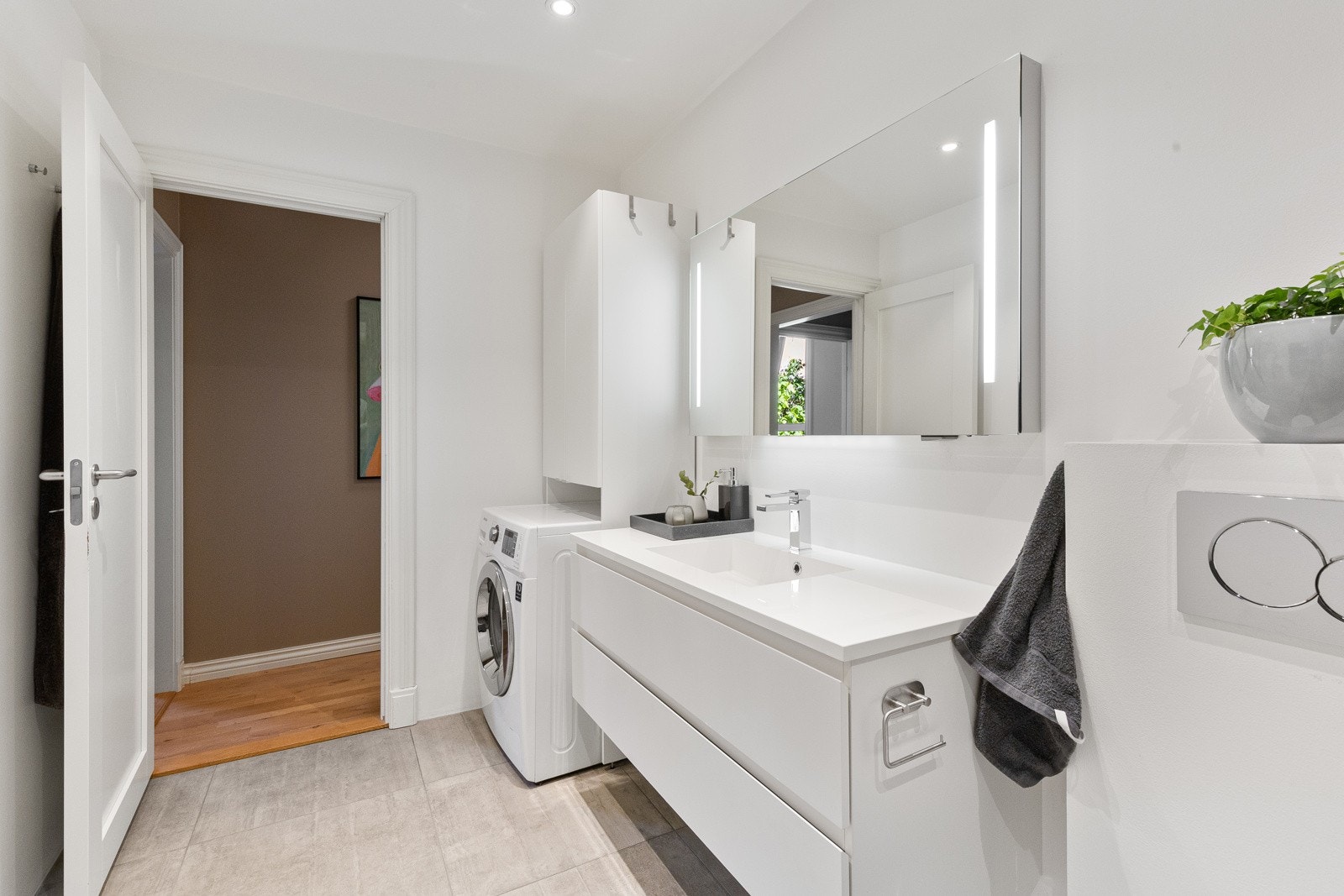 Dusjsonen er romslig og har både regnfallsdusj og hånddusj, samt glassvegg og mosaikkfliser på gulvet. Videre er det vegghengt servantinnredning med hvite fronter og to dype skuffer, veggmontert toalett fra Villeroy & Boch, samt opplegg for vaskemaskin. Galleribilde