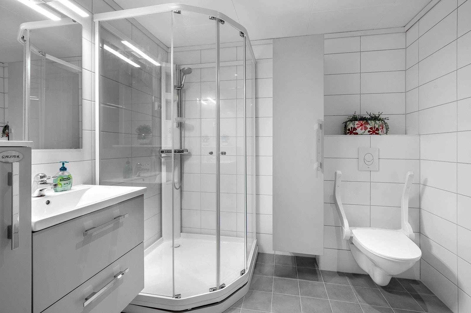 Badet er utstyrt med vegghengt toalett, dusjkabinett og nedfelt servant med skuffer og sideskap. Galleribilde