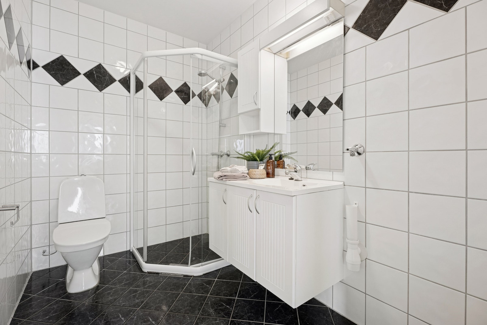 Badet er innredet med servant med underskap, speil med belysning, et gulvmontert toalett og en plassbesparende dusjnisje. Galleribilde