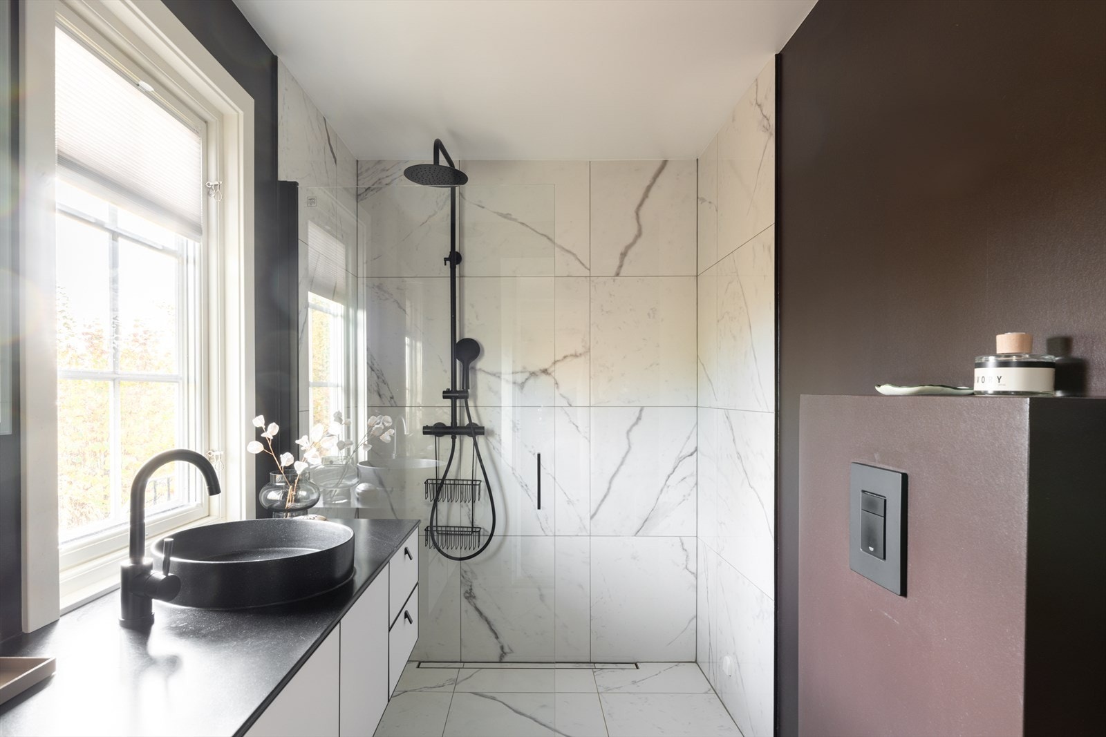 Begge badene ble pusset opp i 2021, og holder en god standard med moderne materialer og fargevalg. Store, hvite gulvfliser i marmormønster kombineres med matchende veggfliser og veggflater malt i en dyp jordtone. Galleribilde