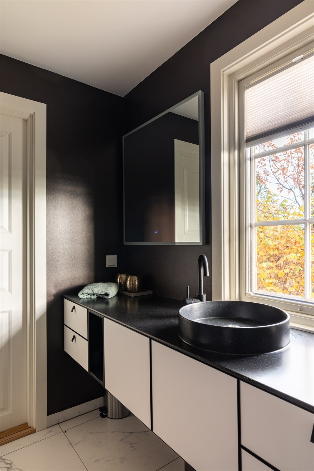 Varme er lagt i gulvet, og begge badene har downlights og vegghengt toalett. Et dusjhjørne er utstyrt med slukrenne, sort regnfallsdusj og en innfellbar dør i herdet glass. Badet har en funksjonell skapseksjon i sort og hvitt med toppmontert servantskål. Galleribilde