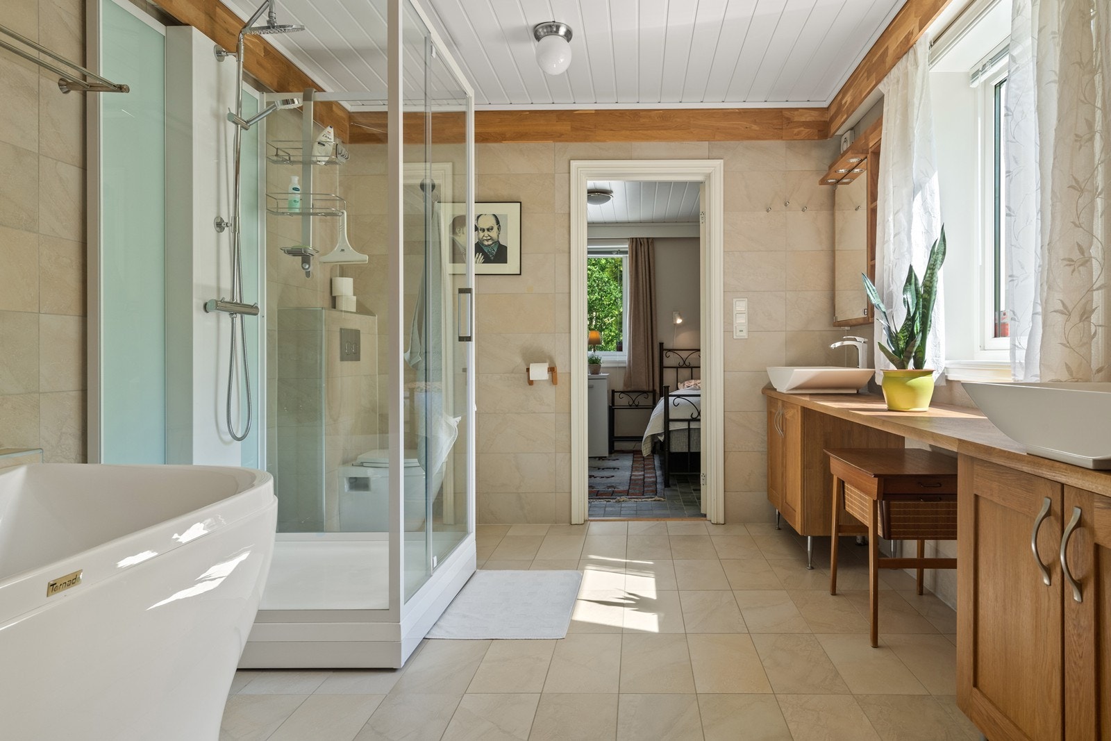 Flislagt bad utstyrt med badekar, dusjkabinett og veggfestet toalett. Galleribilde