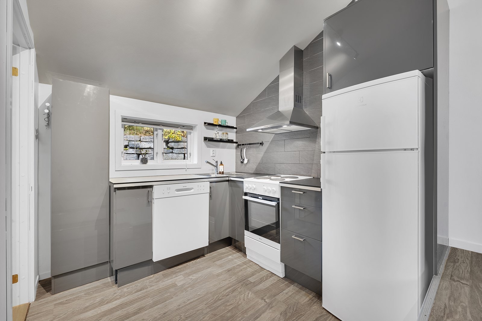 Utleiedelens kjøkken på 9,8 kvm har over- og underskap med folierte fronter, laminat benkeplate, nedfelt oppvaskkum og platetopp. Mekanisk avtrekk og TG1-vurdering fra takstmann. Galleribilde