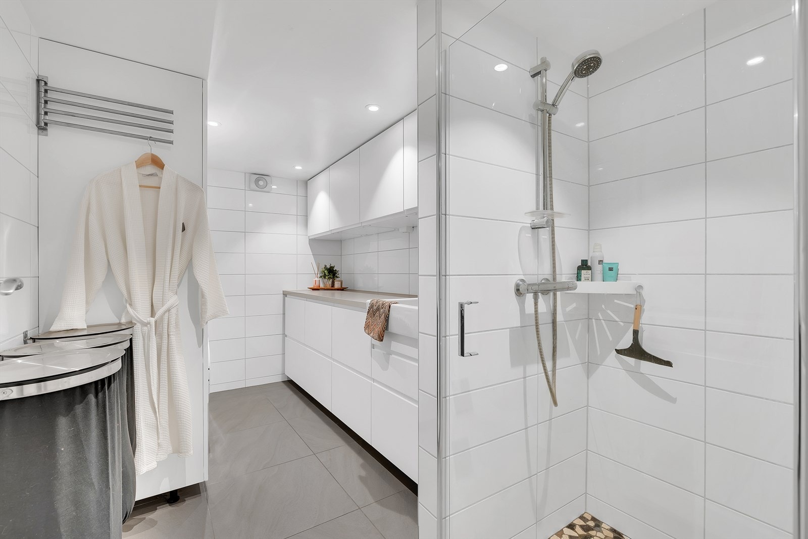 Pent og praktisk bad/vaskerom på ca. 8 kvm, innredet med servant, dusj med glassvegger og dusjgarnityr på vegg. Rommet har også opplegg for vaskemaskin og god plass til oppbevaring. En funksjonell løsning som kombinerer komfort og nytte på elegant vis. Galleribilde