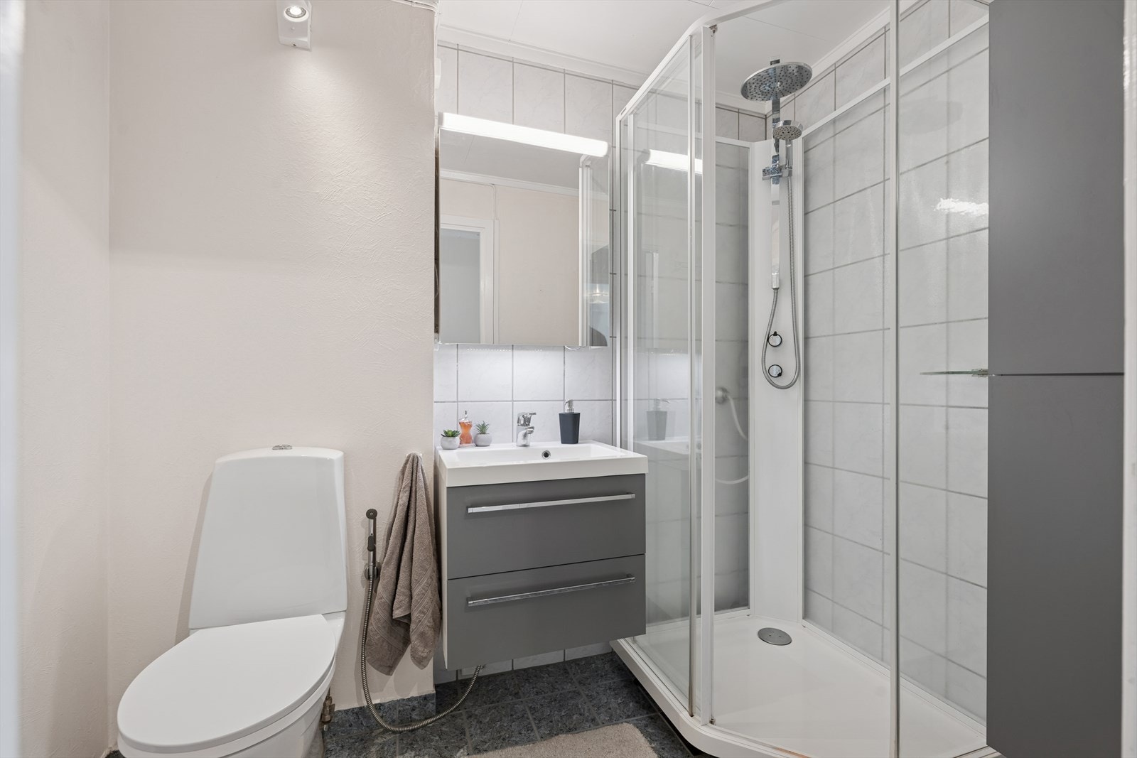 Badet er praktisk innredet, med flislagte gulv utstyrt med behagelige elektriske varmekabler. Rommet er utstyrt med en nedfelt servant, toalett og dusjkabinett, noe som sikrer god komfort og brukervennlighet i hverdagen. Galleribilde