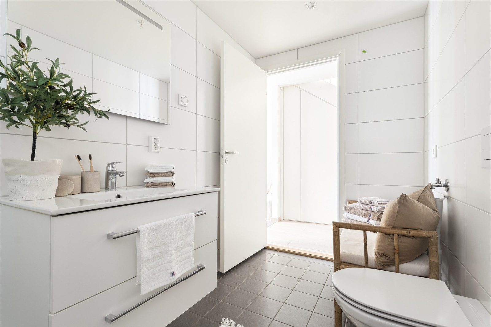 Delikat flislagt baderom med gulvvarme, servantinnredning, speil med lys, dusjhjørne med dusjvegger og vegghengt toalett. Galleribilde