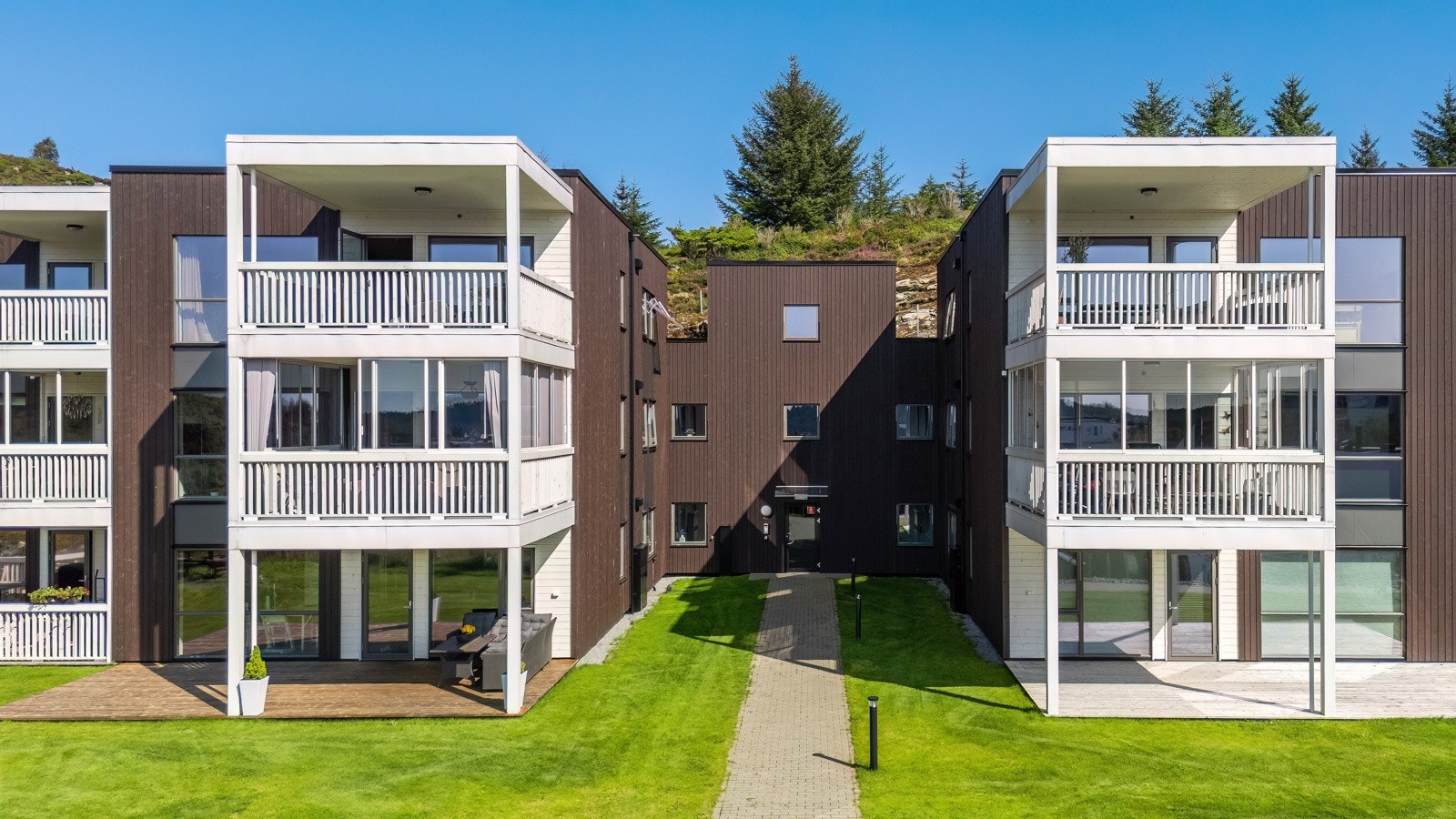 Felles tomt for borettslaget som er pent opparbeidet med beplantning, plen, hyggelige gangveier, sittegrupper og gjesteparkering. Galleribilde