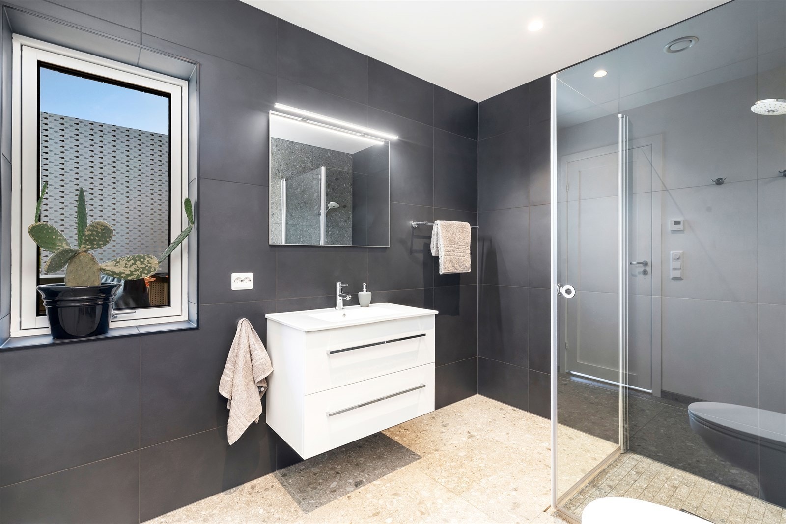 Baderommet i etasjen er flislagt med dusjhjørne, vegghent toalett, servant med oppbevaring samt egen vaskeromsløsning. Galleribilde