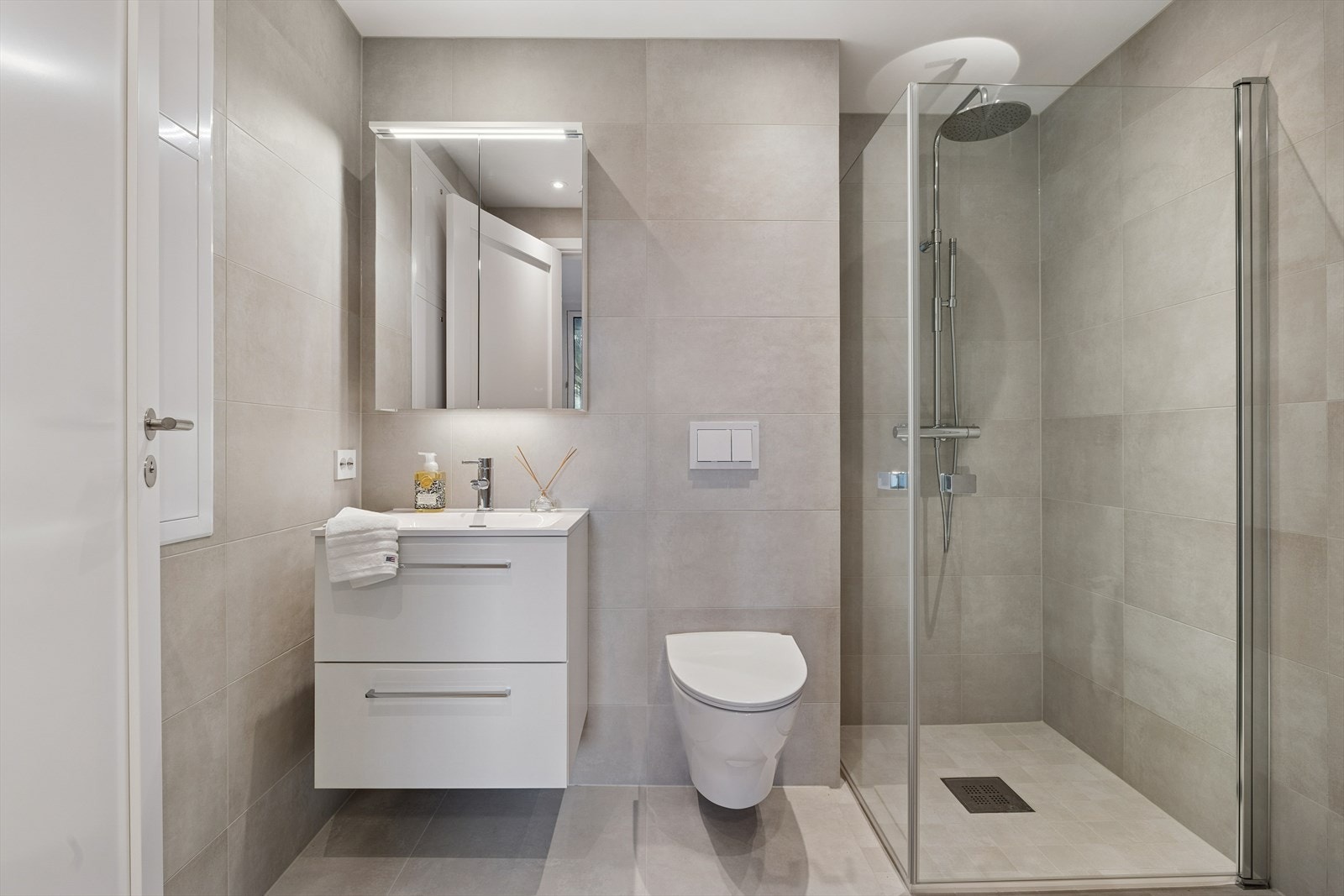 Badet er delikat innredet med grå fliser, dusjhjørne, vegghengt toalett og opplegg for vaskemaskin. Galleribilde