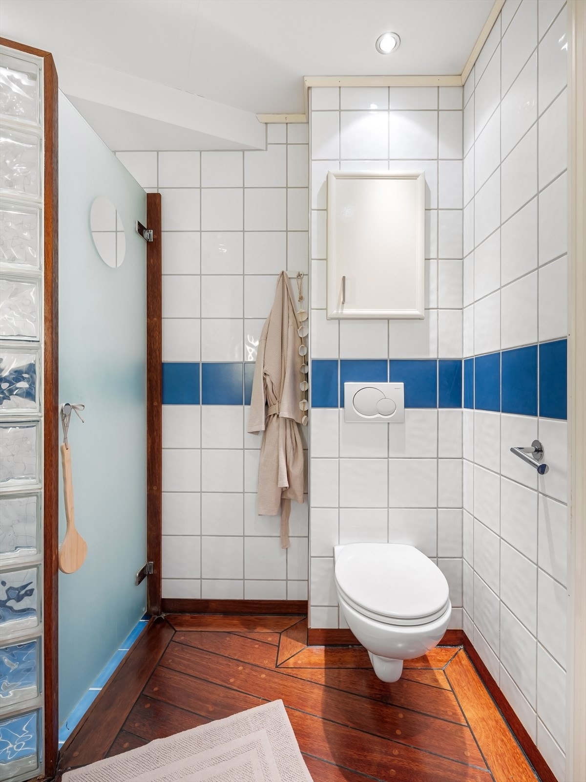 Badet inneholder skjermet dusjhjørne med delevegg med glass felt og innfellbar glassdør, veggmontert toalett og baderomsinnredning med skuffer, nedfelt servant med ettgreps armatur og speil med lys på veggen. Galleribilde