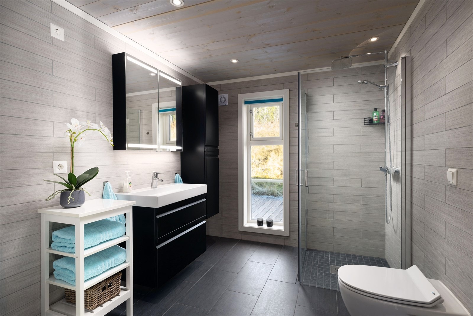 Badet har fliser på gulv og vegg, og varmekabler i gulvet. Innredet med dusjnisje, servantinnredning, vegghengt høyskap, vegghengt Jets vannklosett. Opplegg for vaskemaskin og tørketrommel. Galleribilde