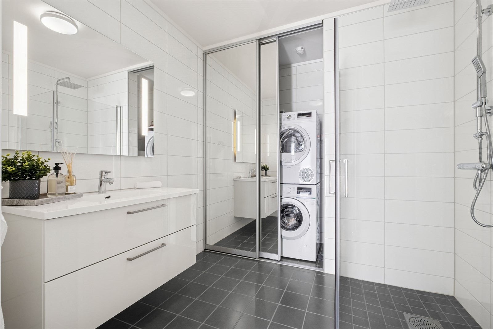 Moderne og flislagt baderom med opplegg for vaskemaskin/tørketrommel - praktisk gjemt bak skyvedører med speil. Galleribilde