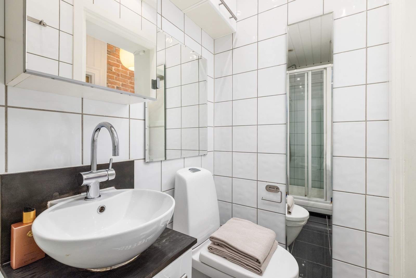 Plassert under et speilskap i 2018 har badet en hvit skapseksjon med toppmontert servantskål. Platen fortsetter opp på veggen, og i en egen nisje er det ekstra oppbevaring i et matchende høyskap. Galleribilde