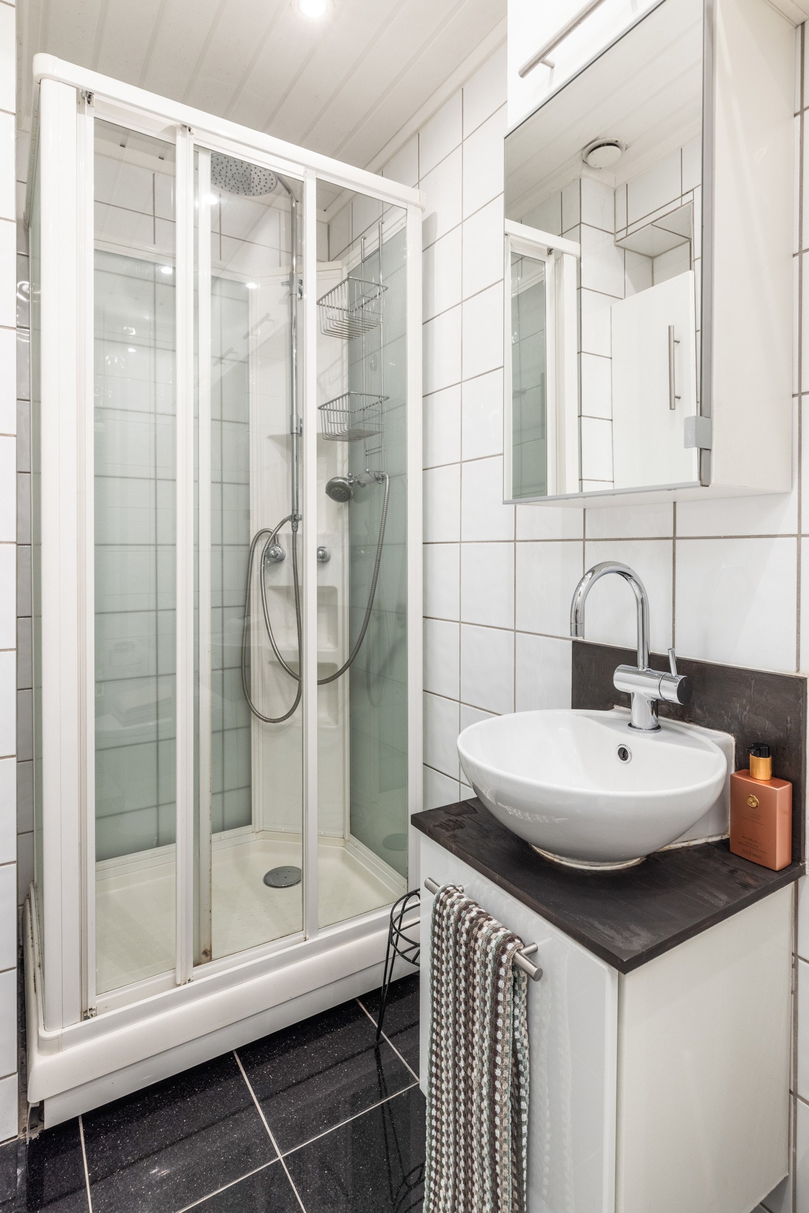 Badet har hvite veggfliser og sorte gulvfliser fra 2011. I 2024 ble badet oppgradert med nytt toalett, nye led-downlights og ny termostat til gulvvarme. Dusjkabinett med regnfallsdusj. Galleribilde