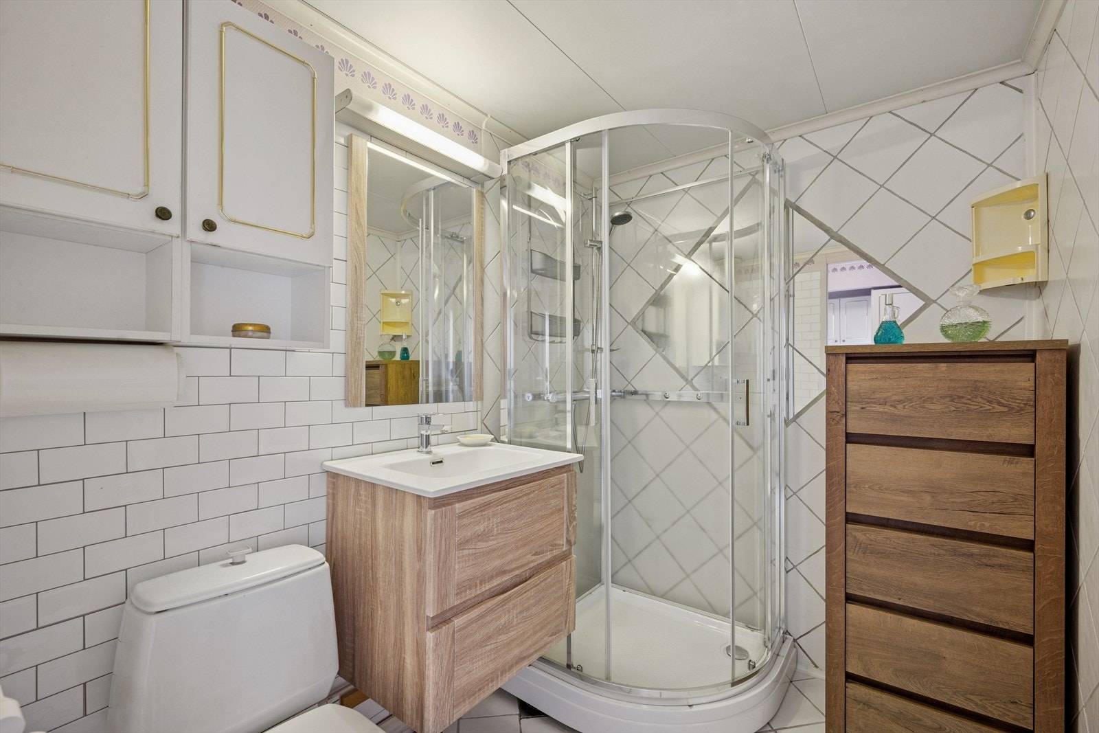 Badet er utstyrt med en baderomsinnredning med glatte fronter, speil og belysning over servant, samt høyskap og veggskap med profilerte fronter. Videre er det en servant i helstøpt plate, dusjkabinett, gulvstående klosett og opplegg for vaskemaskin. Galleribilde