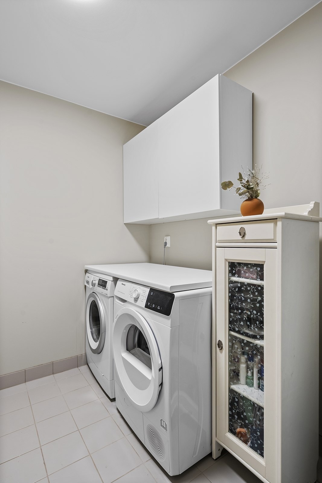 Praktisk vaskerom med med flislagt gulv med varmekabler. Det er opplegg til vaskemaskin og tørketrommel under benkeplate Galleribilde