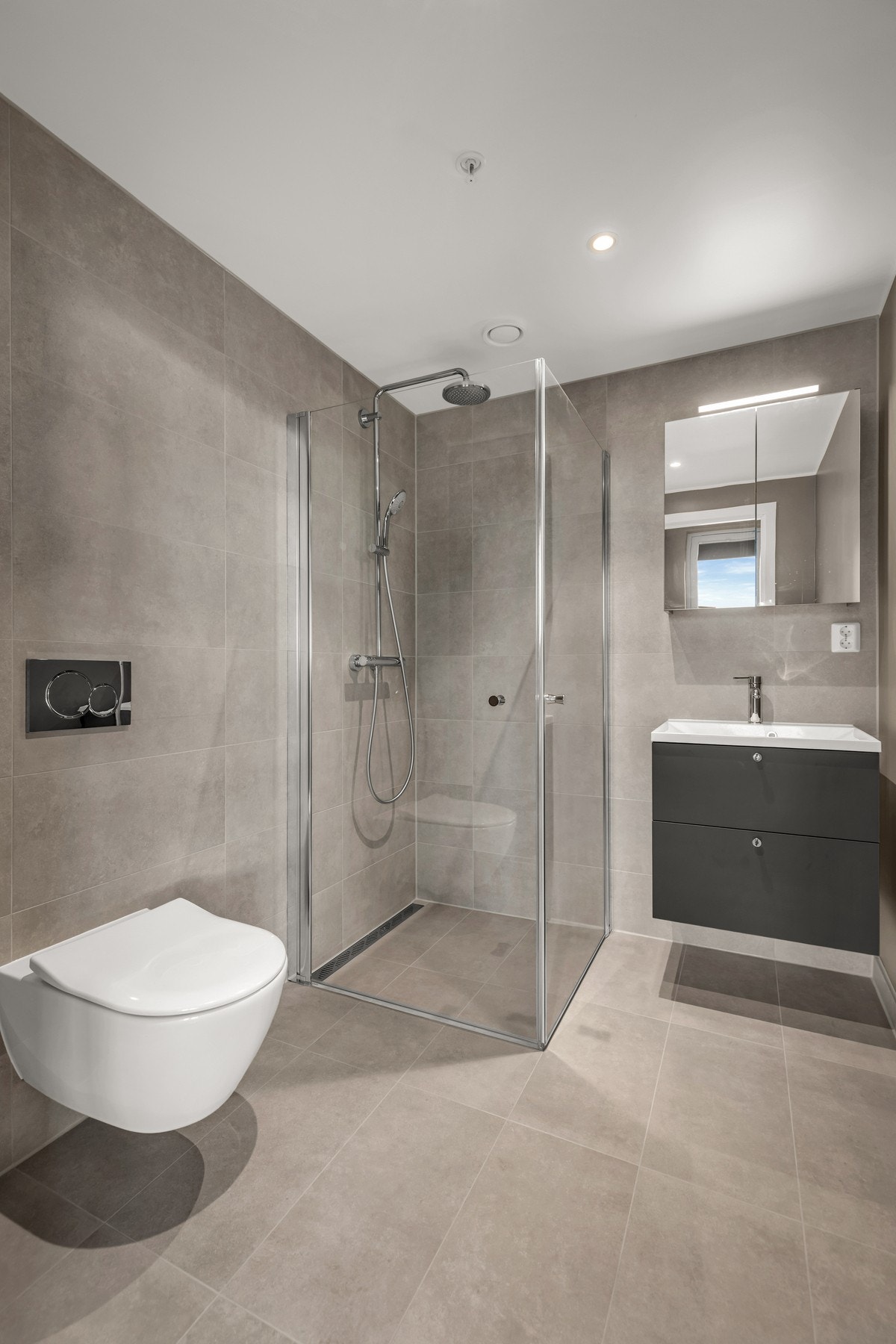 Badet tilknyttet hovedsoverommet er innredet med vegghengt toalett, dusjhjørne med innfellbare glassvegger og servant med skuffer under og speilskap over. Galleribilde