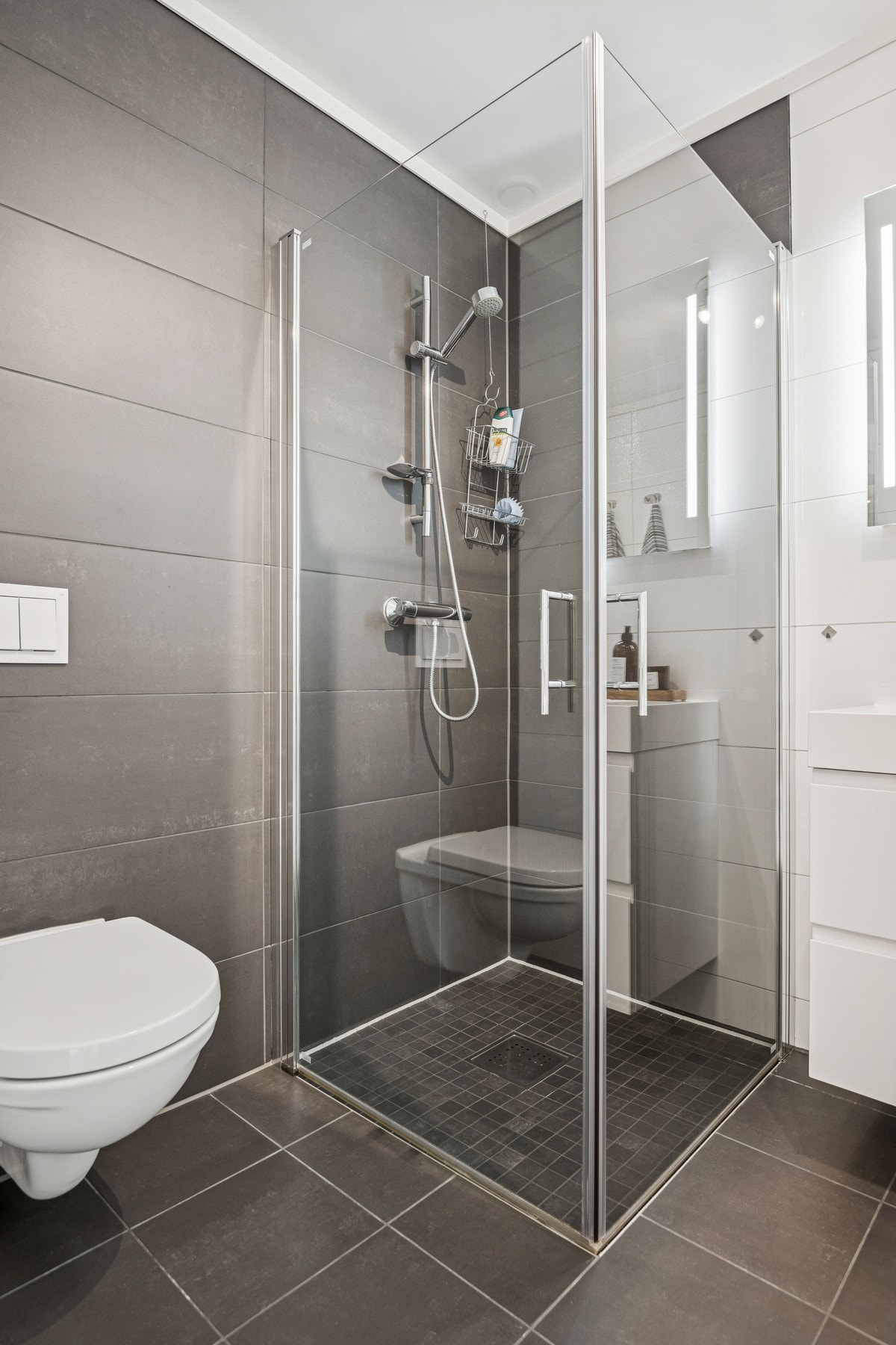 Her finner du dusjhjørne med glassdører, vegghengt toalett og servant med underskap. Galleribilde